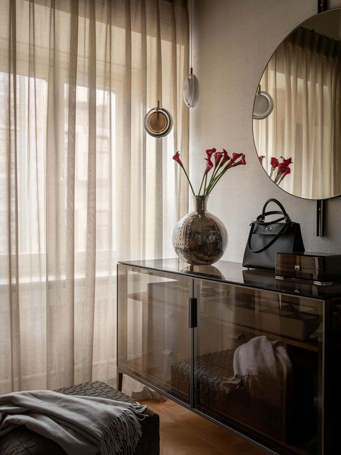 A cozy interior featuring sheer curtains, a vase with red flowers, sleek furniture, and a stylish handbag on a glass console. A cozy interior featuring sheer curtains, a vase with red flowers, sleek furniture, and a stylish handbag on a glass console.