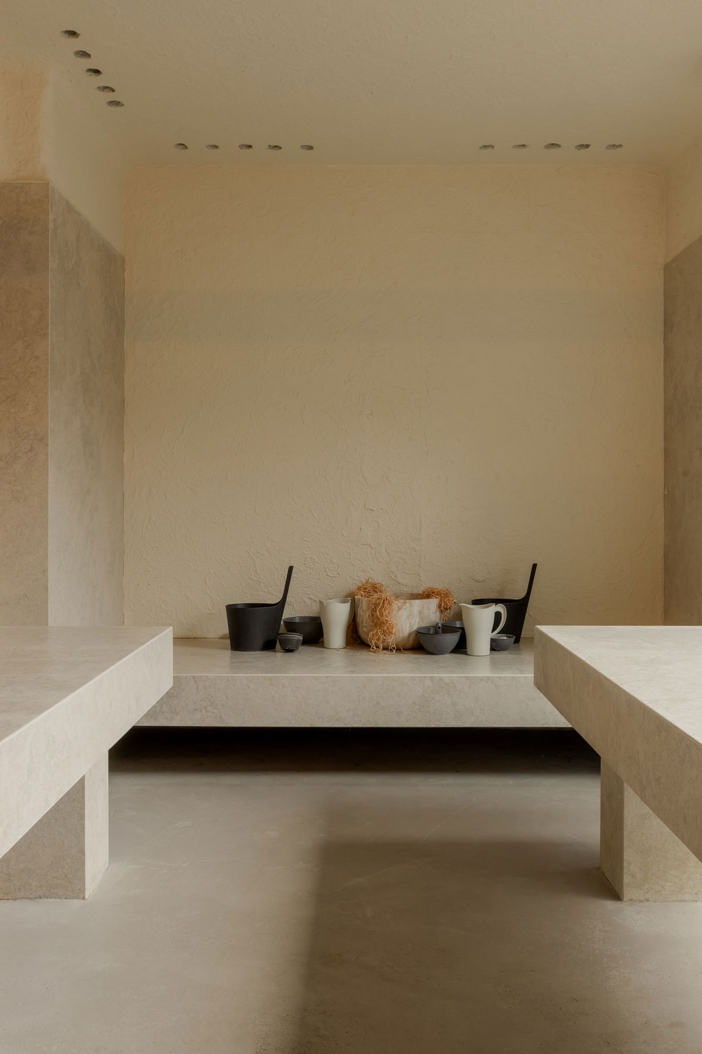 Minimalist interior featuring two stone benches, soft lighting, and a collection of simple pottery on display against a textured wall.