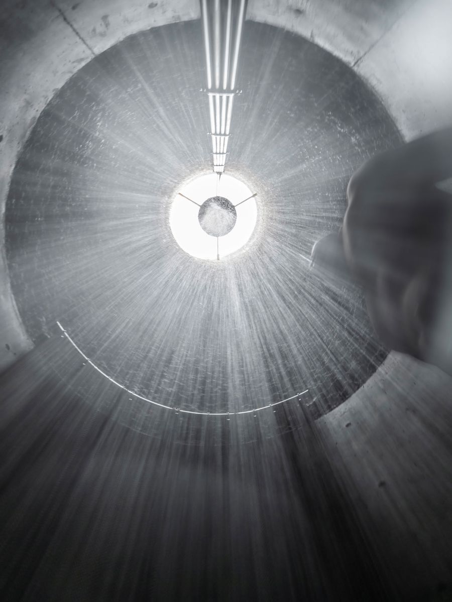 Looking up a circular concrete shaft, illuminated by bright light, with rays of light and water cascading down into the darkness. Looking up a circular concrete shaft, illuminated by bright light, with rays of light and water cascading down into the darkness.