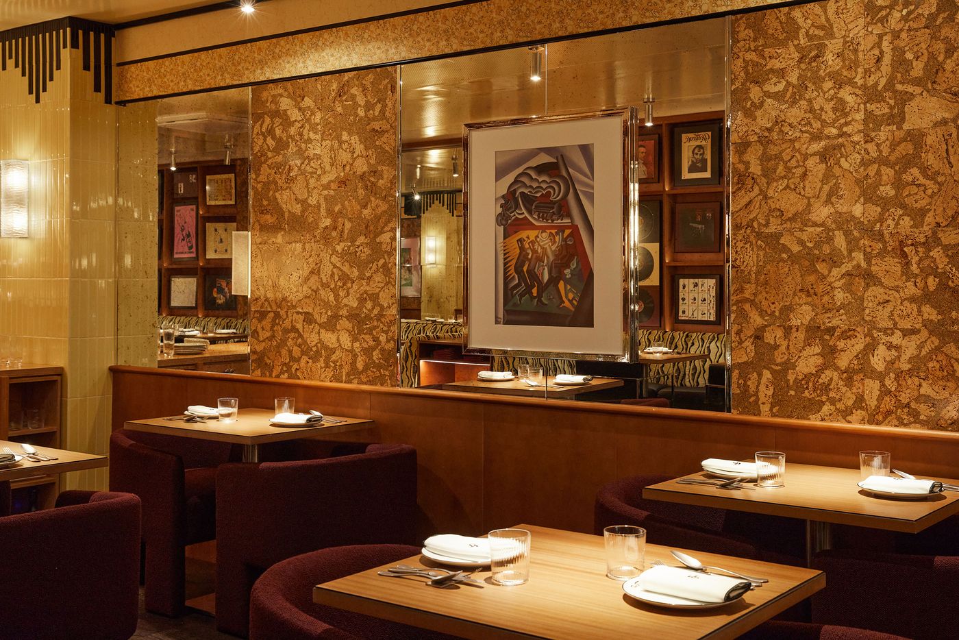 This view of the dining room showcases an eclectic, maximalist design with bold textural contrasts. The walls feature a decorative, cork-like finish and sections of reflective mirror. Upholstered banquettes in a rich burgundy color invite guests, while a prominent, centrally-placed painting adds an artistic focal point. This view of the dining room showcases an eclectic, maximalist design with bold textural contrasts. The walls feature a decorative, cork-like finish and sections of reflective mirror. Upholstered banquettes in a rich burgundy color invite guests, while a prominent, centrally-placed painting adds an artistic focal point.
