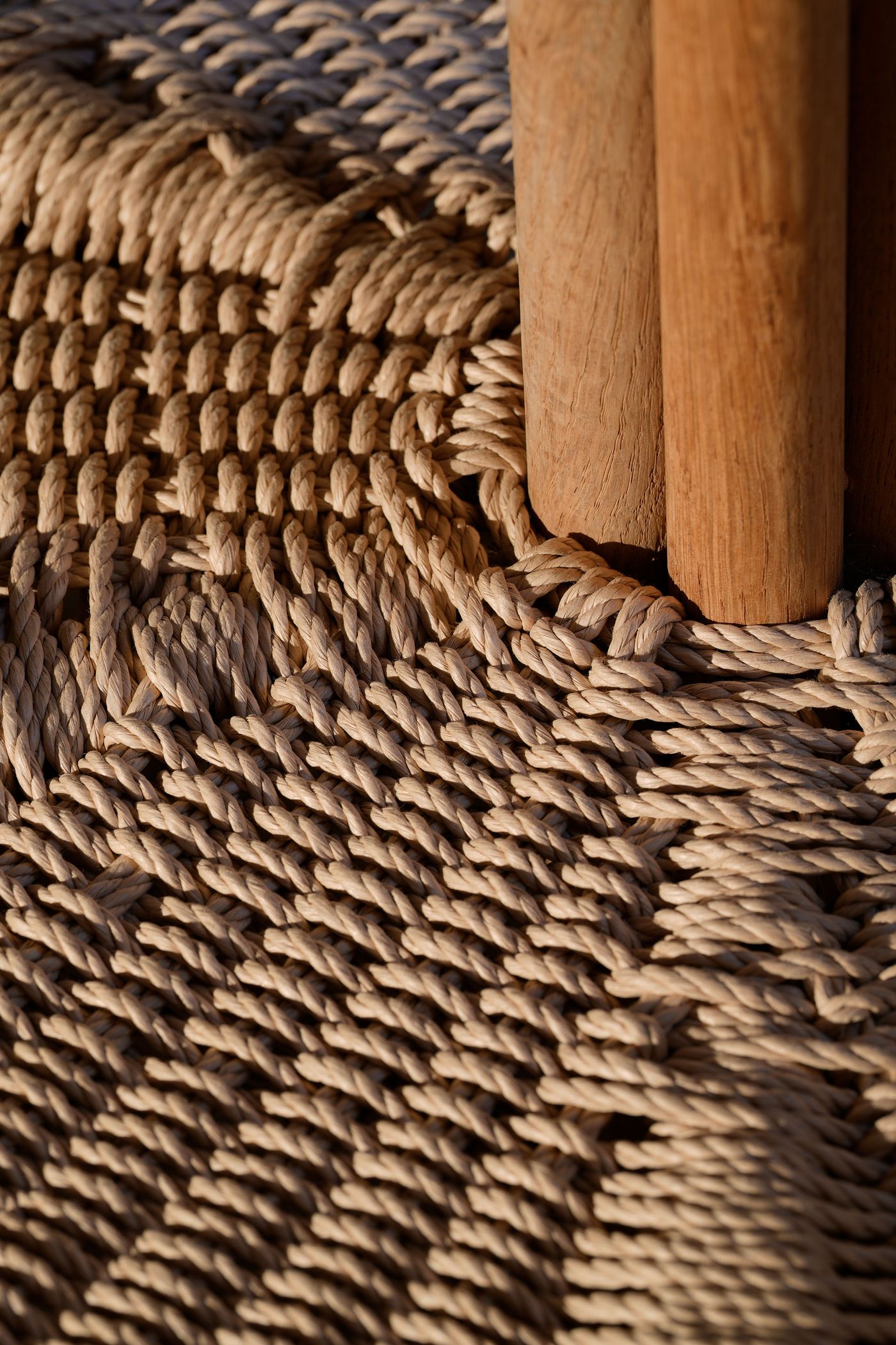 Close-up of woven natural rope on a surface, with wooden legs partially visible, highlighting intricate textures and earthy tones. Close-up of woven natural rope on a surface, with wooden legs partially visible, highlighting intricate textures and earthy tones.
