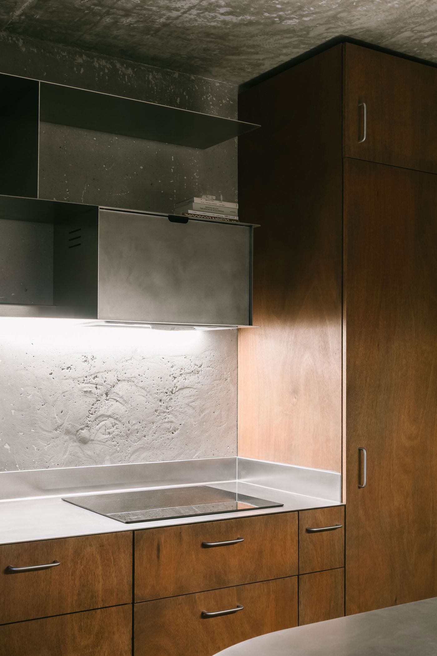 Modern kitchen with sleek wooden cabinets, minimalist metal accents, and a concrete wall, featuring a glass induction cooktop. Modern kitchen with sleek wooden cabinets, minimalist metal accents, and a concrete wall, featuring a glass induction cooktop.