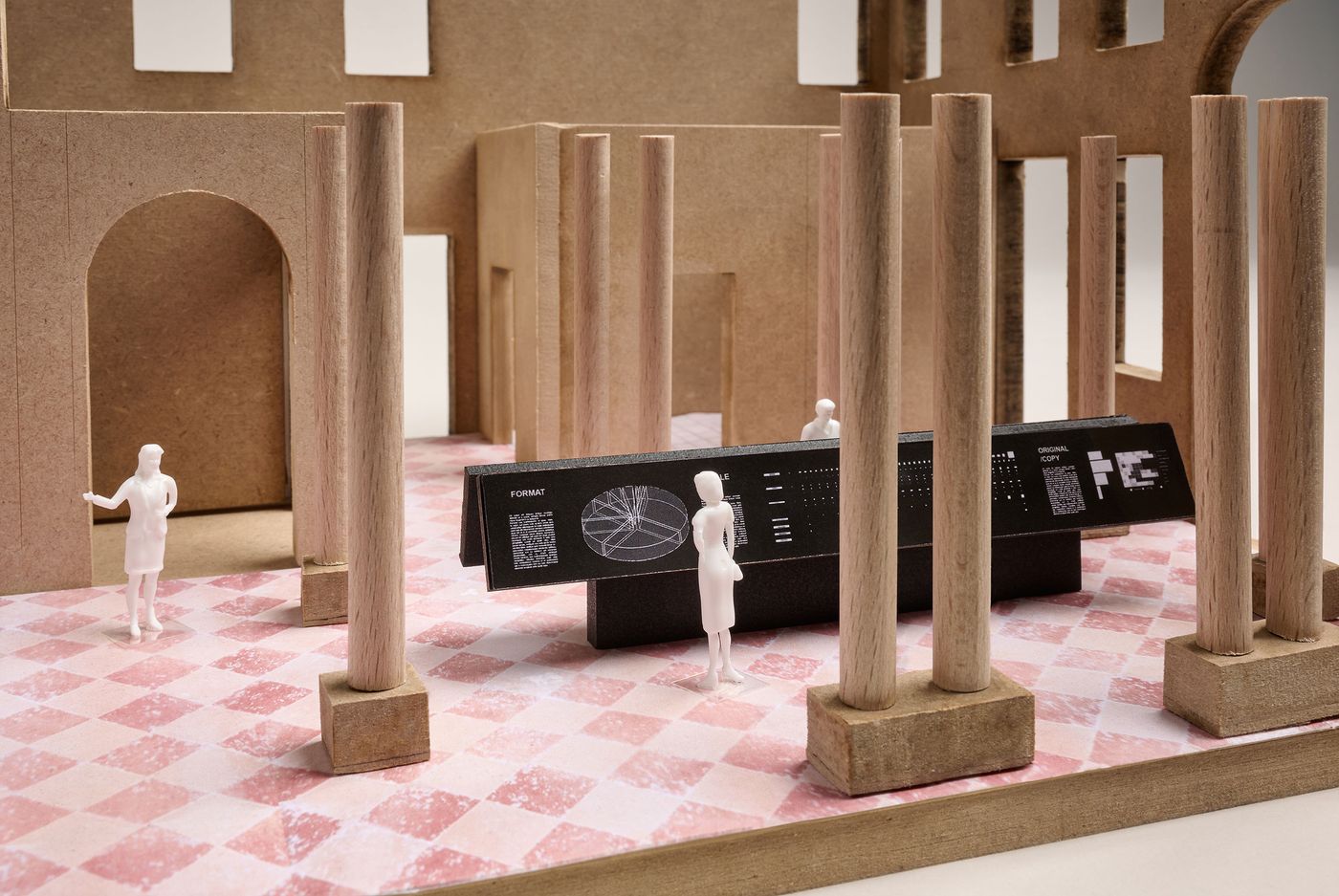 A miniature architectural model featuring columns, a patterned floor, and small figures interacting with a digital display. A miniature architectural model featuring columns, a patterned floor, and small figures interacting with a digital display.
