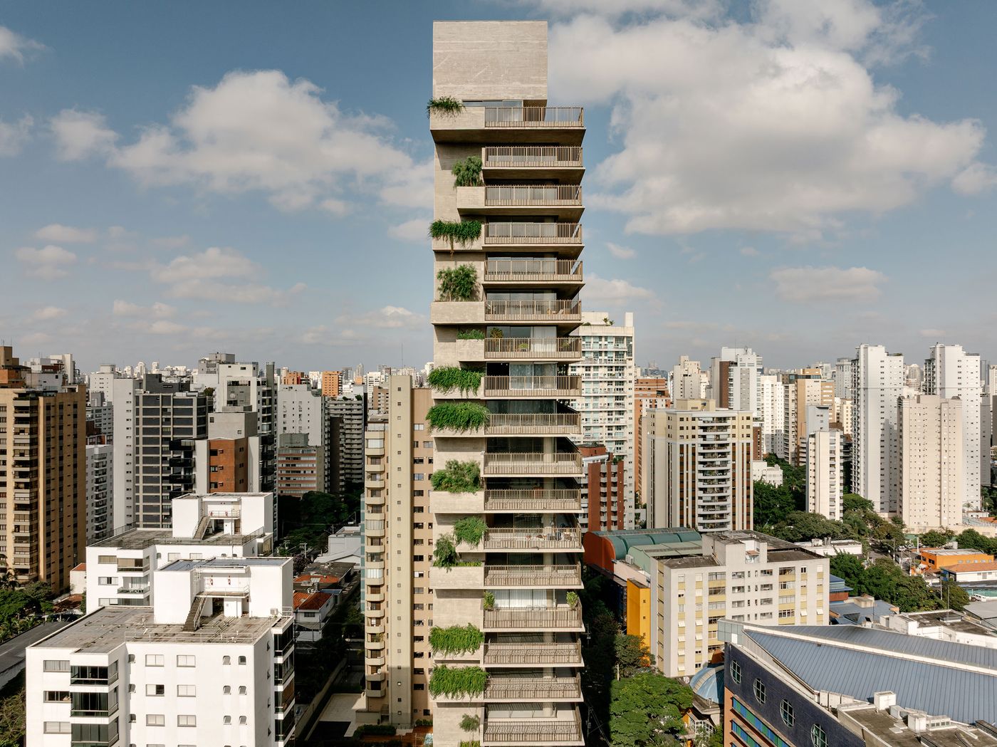 A wide shot of the Ibaté residential tower, a beacon of biophilic brutalism designed by Studio Arthur Casas, standing tall amidst the urban fabric of São Paulo. Its concrete balconies are rich with integrated greenery, showcasing a harmonious blend of nature and modern architecture.