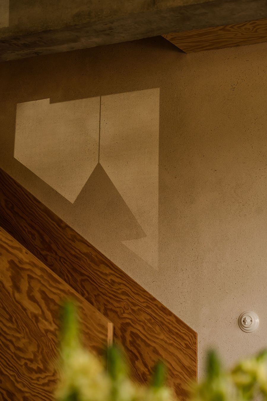 A close-up of a staircase where a geometric shadow casts on a smooth, light-colored wall, complemented by warm wood textures. A close-up of a staircase where a geometric shadow casts on a smooth, light-colored wall, complemented by warm wood textures.