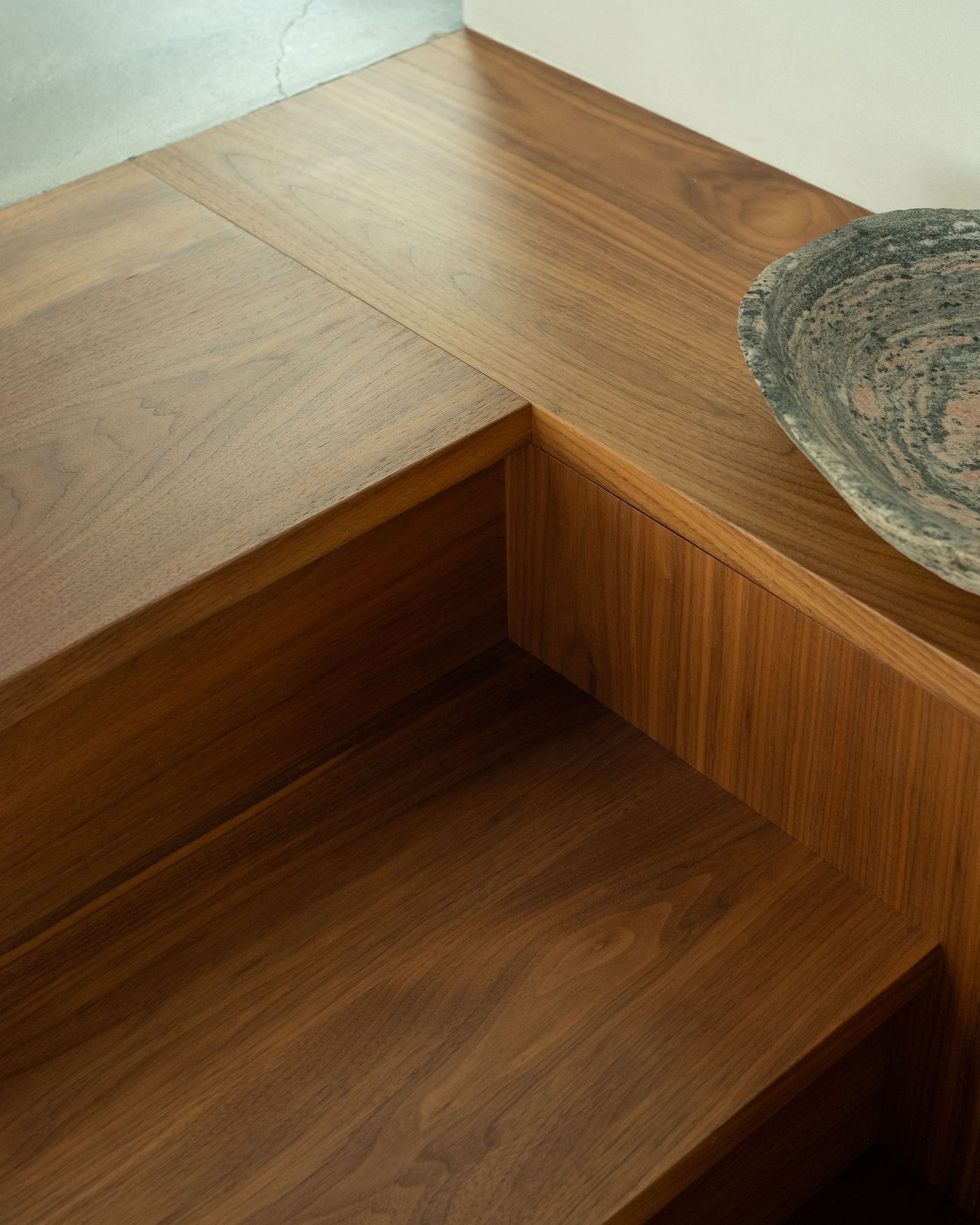 Close-up of polished wooden stairs, featuring rich walnut tones, with a textured ceramic bowl resting on the upper surface.
