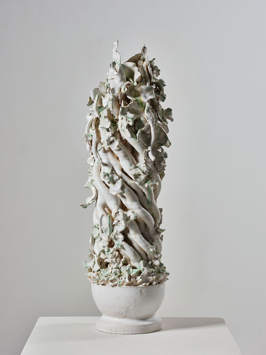 A tall, twisting white sculpture with green accents, resembling entwined vines, displayed on a pedestal against a light backdrop. A tall, twisting white sculpture with green accents, resembling entwined vines, displayed on a pedestal against a light backdrop.