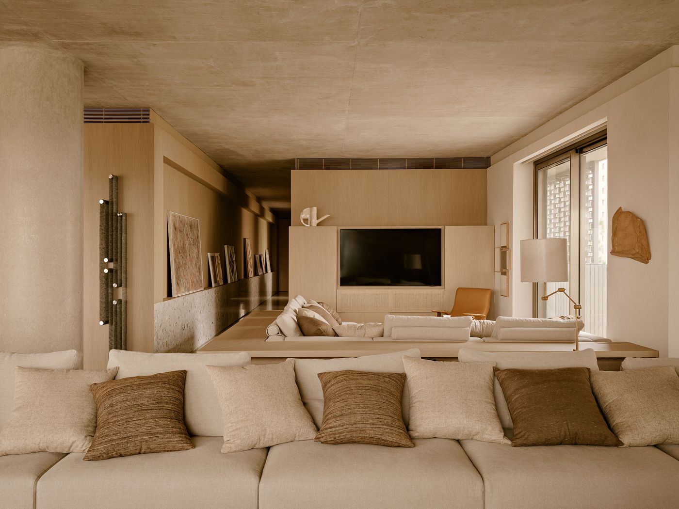 A modern living room with a beige sofa adorned with textured pillows, a flat-screen TV, wooden accents, and large windows for natural light. A modern living room with a beige sofa adorned with textured pillows, a flat-screen TV, wooden accents, and large windows for natural light.
