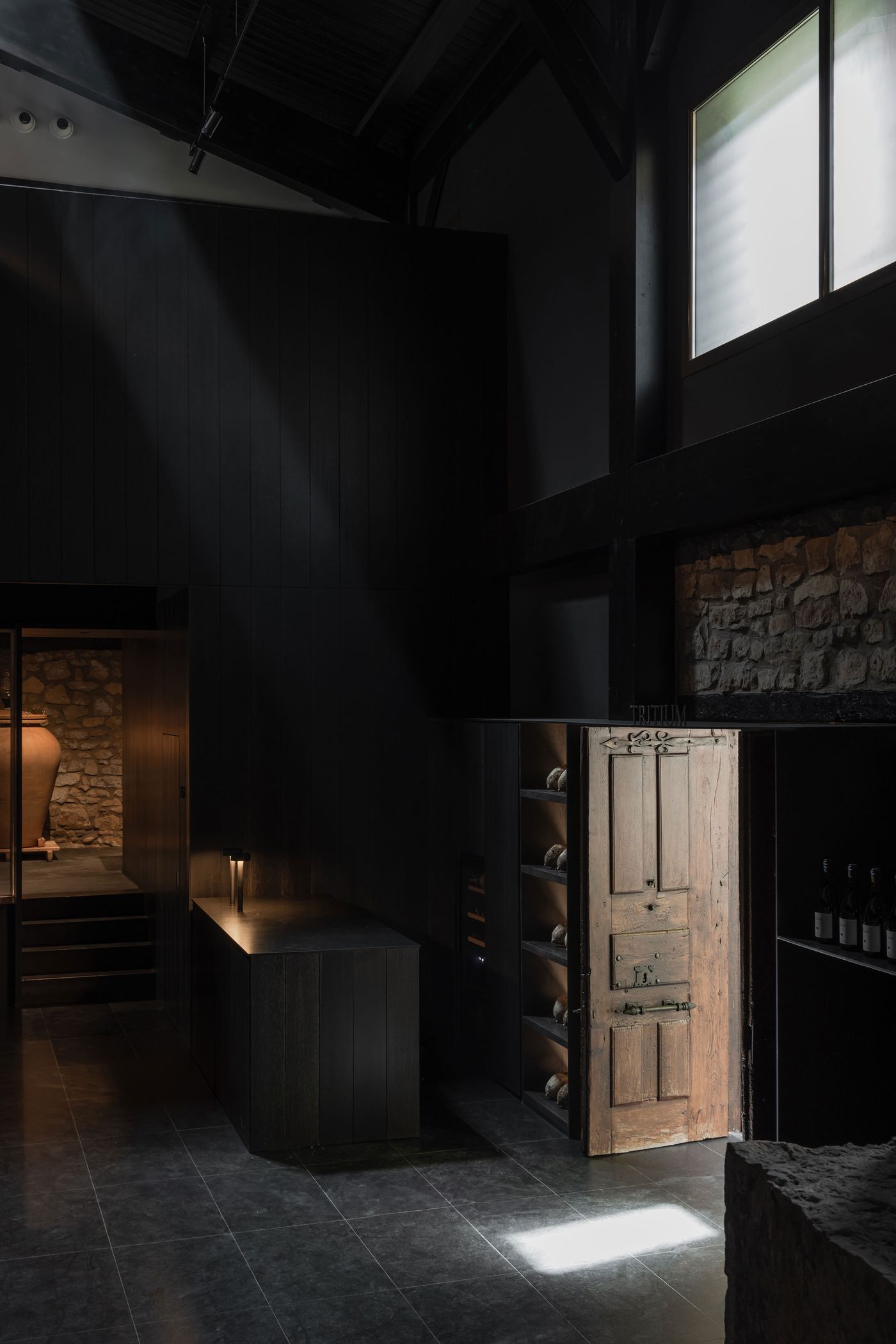 Interior of a dimly lit modern space featuring dark wooden walls, stone accents, a vintage door, and a spotlight illuminating the floor. Interior of a dimly lit modern space featuring dark wooden walls, stone accents, a vintage door, and a spotlight illuminating the floor.