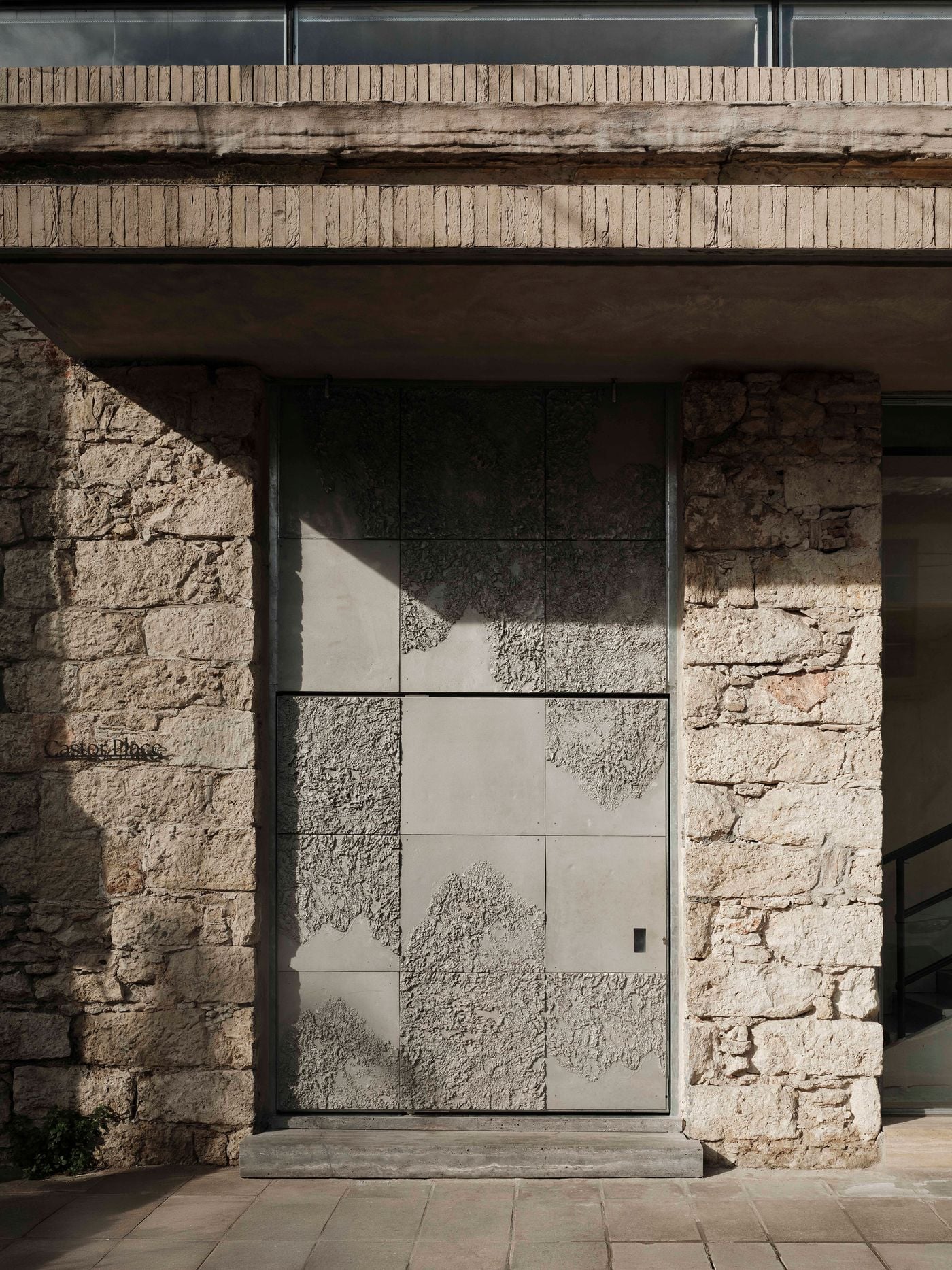 Castor Place’s entrance is set within the retained stone façade, marked by a monumental metal door composed of smooth and heavily textured aluminium panels. The irregular relief echoes the weathered masonry surrounding it, establishing MPNYC’s strategy of translating the building’s existing material character into contemporary elements. Castor Place’s entrance is set within the retained stone façade, marked by a monumental metal door composed of smooth and heavily textured aluminium panels. The irregular relief echoes the weathered masonry surrounding it, establishing MPNYC’s strategy of translating the building’s existing material character into contemporary elements.