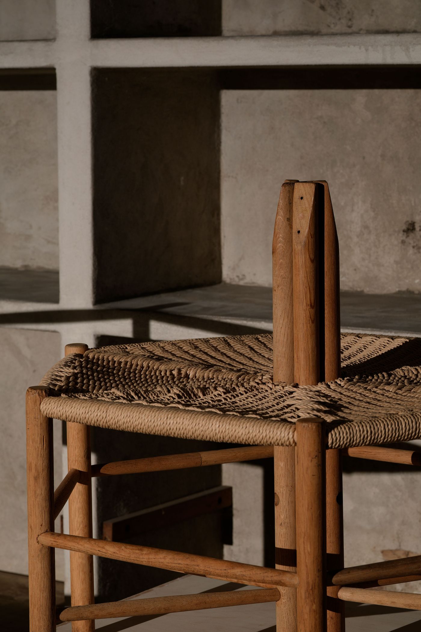A wooden chair with a woven straw seat sits against a textured concrete wall, showcasing minimalist design and warm tones. A wooden chair with a woven straw seat sits against a textured concrete wall, showcasing minimalist design and warm tones.