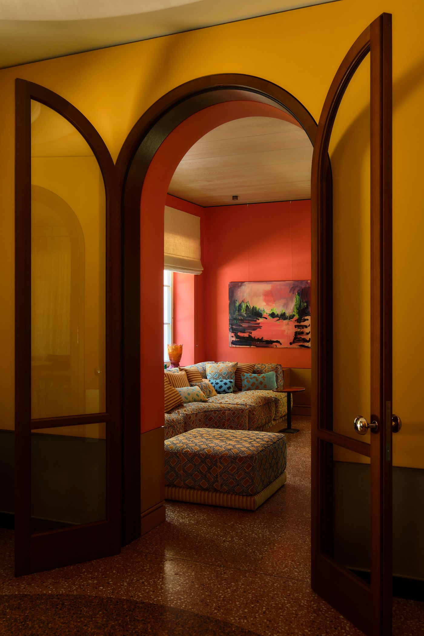 A view through arched doors into a vibrant living room with patterned seating, colorful walls, and a bright artwork. A view through arched doors into a vibrant living room with patterned seating, colorful walls, and a bright artwork.