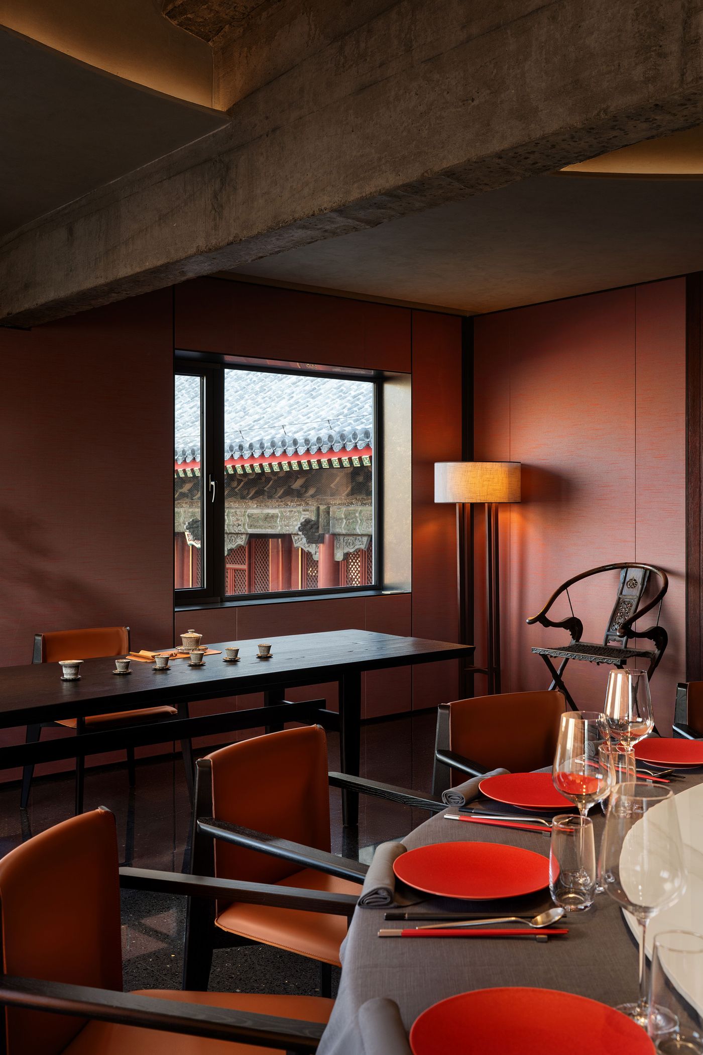 A modern dining room with orange chairs, a black table set for a meal, and a window showcasing traditional architecture outside. A modern dining room with orange chairs, a black table set for a meal, and a window showcasing traditional architecture outside.