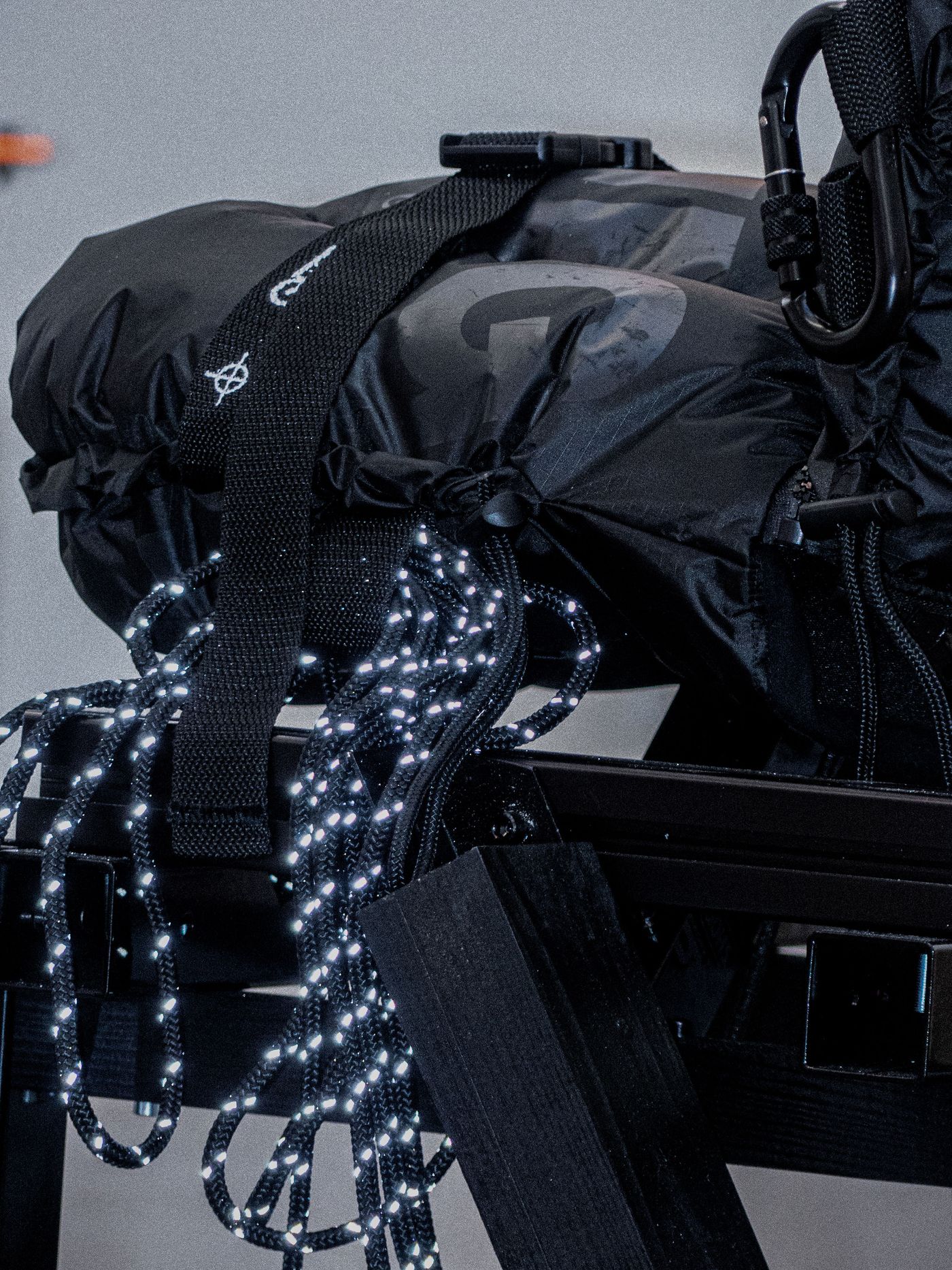 A close-up of a black backpack secured with straps and illuminated cords, resting on a wooden surface. A close-up of a black backpack secured with straps and illuminated cords, resting on a wooden surface.