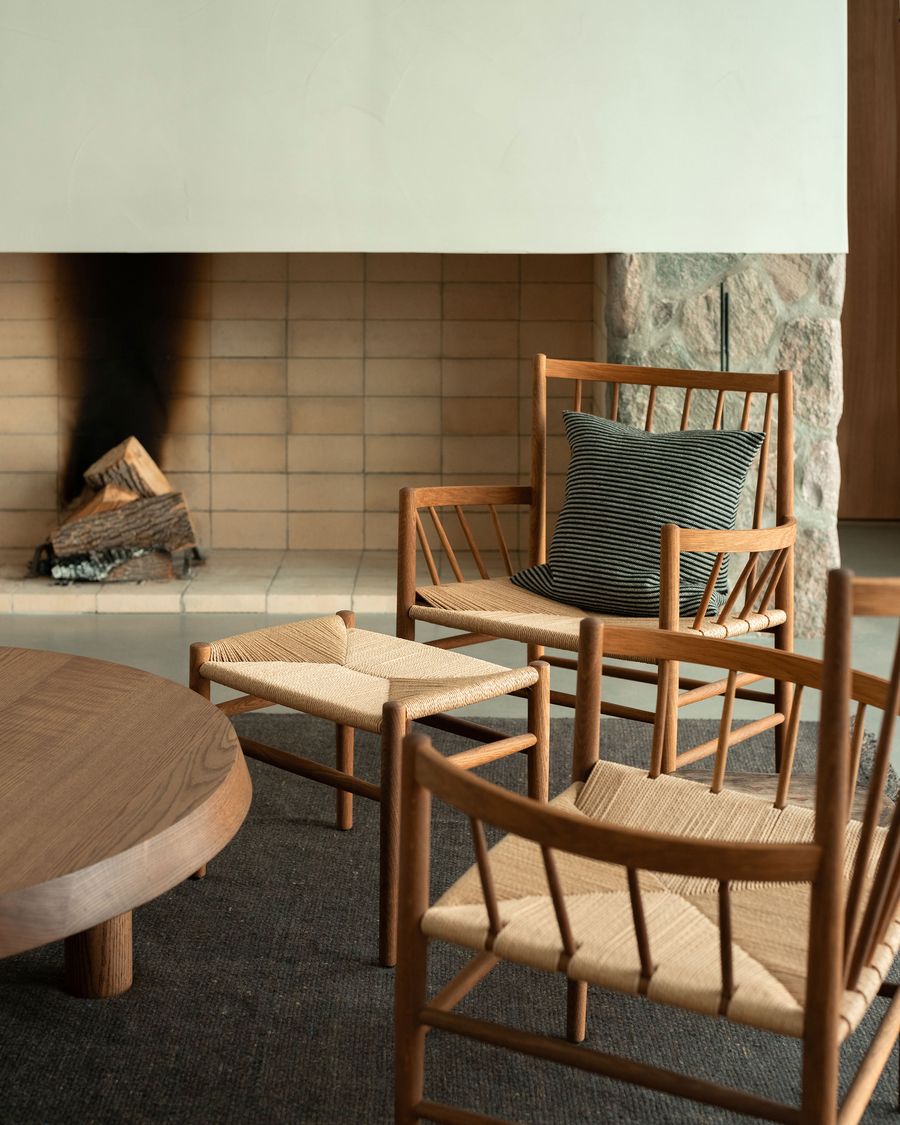 A cozy living room featuring wooden chairs and a low round table, beside a tiled fireplace with stacked logs, exuding warmth and comfort. A cozy living room featuring wooden chairs and a low round table, beside a tiled fireplace with stacked logs, exuding warmth and comfort.