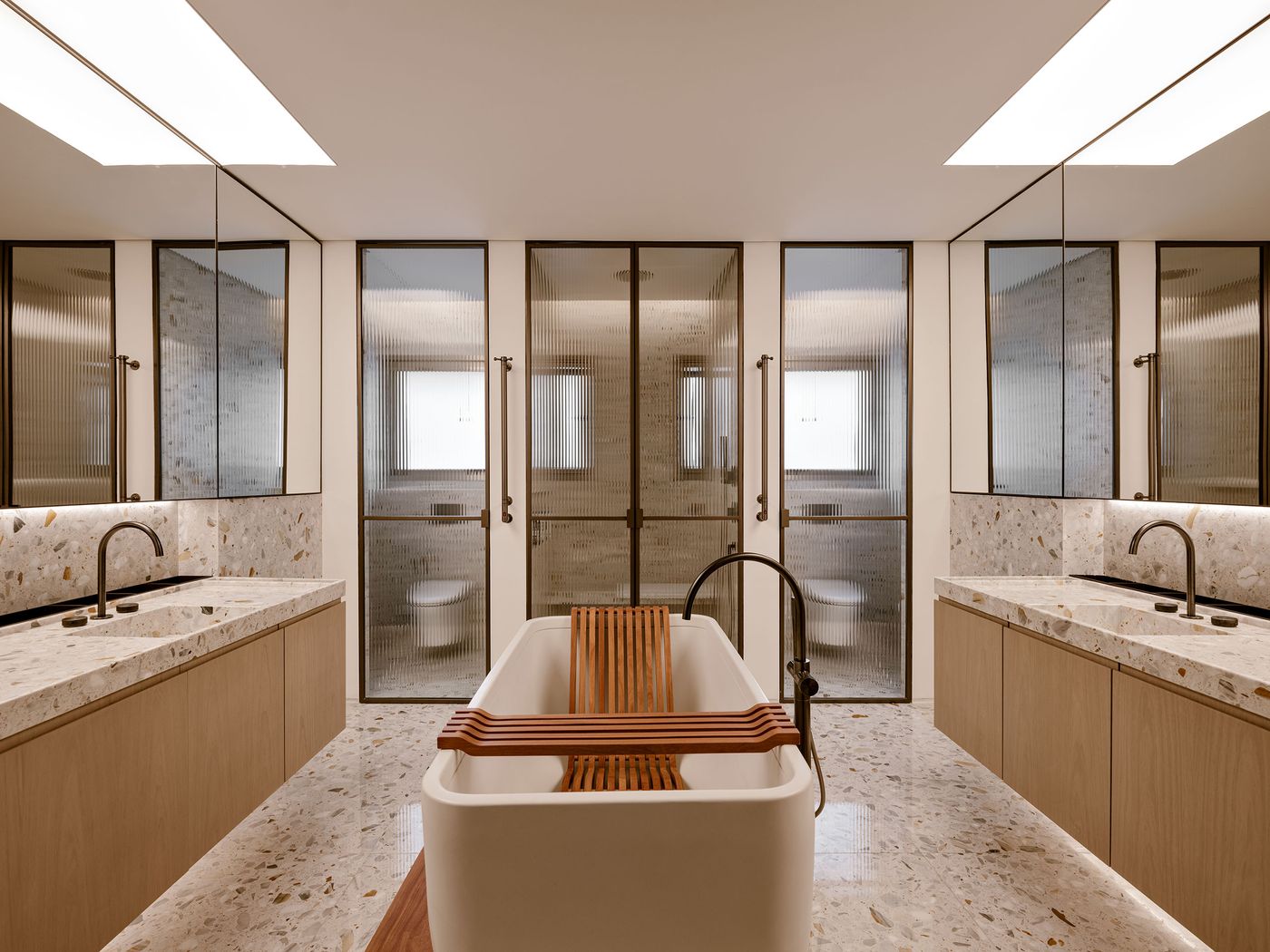 Luxurious modern bathroom with a freestanding tub, dual vanities, and frosted glass doors, accented by warm wood and marble surfaces. Luxurious modern bathroom with a freestanding tub, dual vanities, and frosted glass doors, accented by warm wood and marble surfaces.
