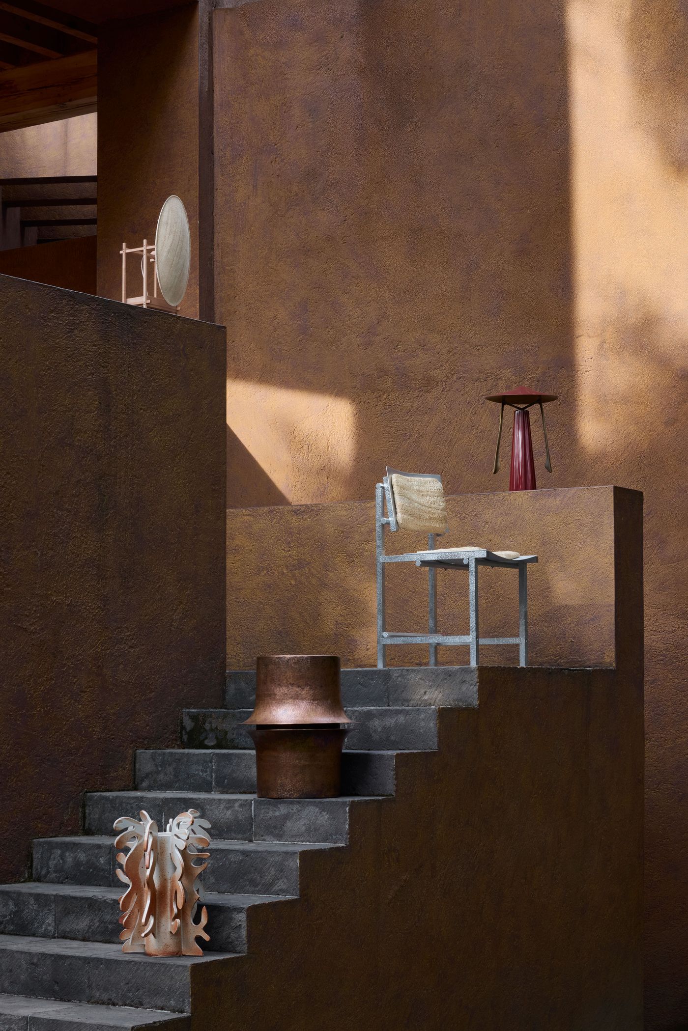A modern staircase features artistic furniture pieces: a silver chair, a copper pot, a red lamp, and a sculptural object, all against warm-toned walls.