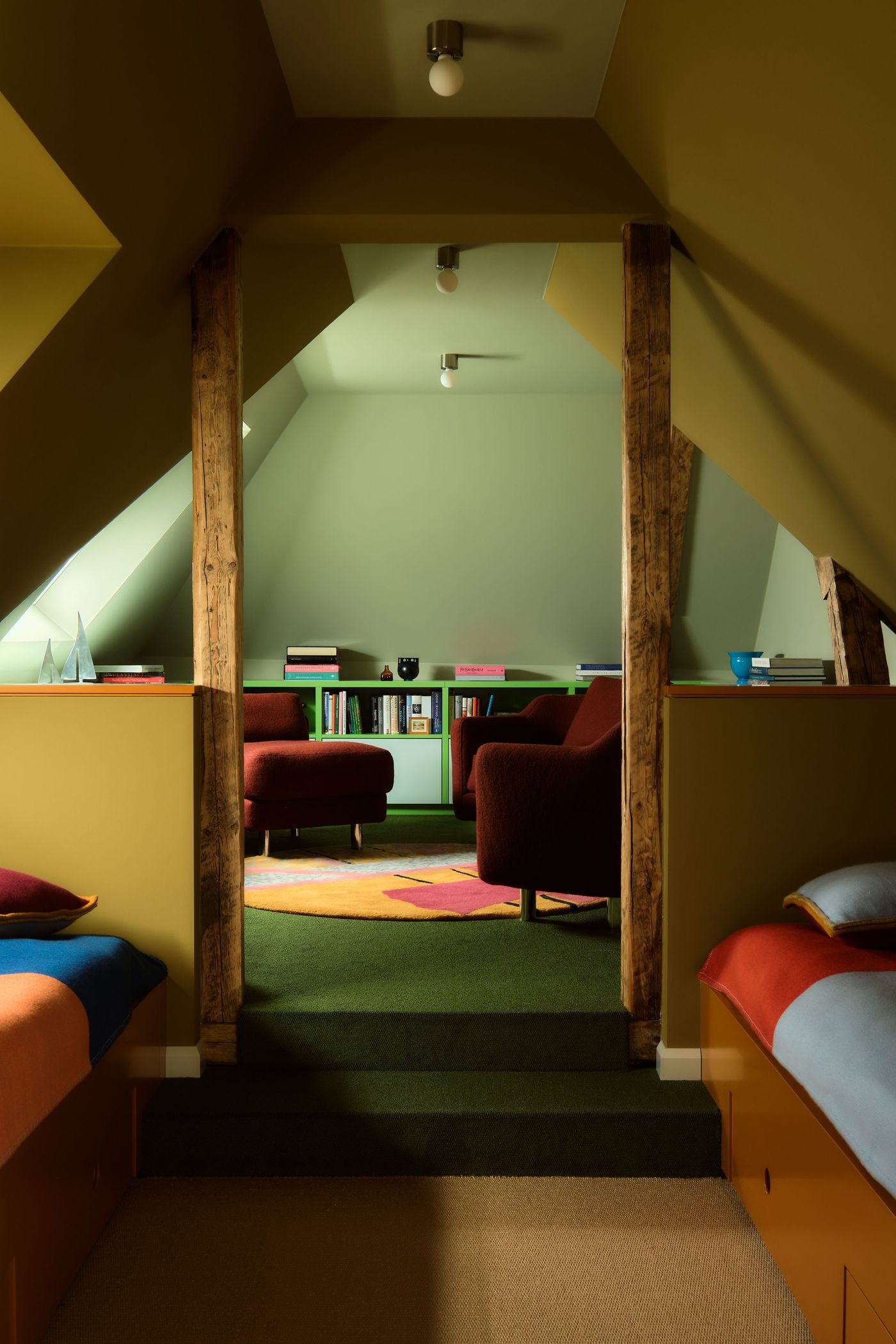 Cozy attic lounge featuring green walls, two brown chairs, a colorful rug, and wooden beams, illuminated by soft ceiling lights. Cozy attic lounge featuring green walls, two brown chairs, a colorful rug, and wooden beams, illuminated by soft ceiling lights.