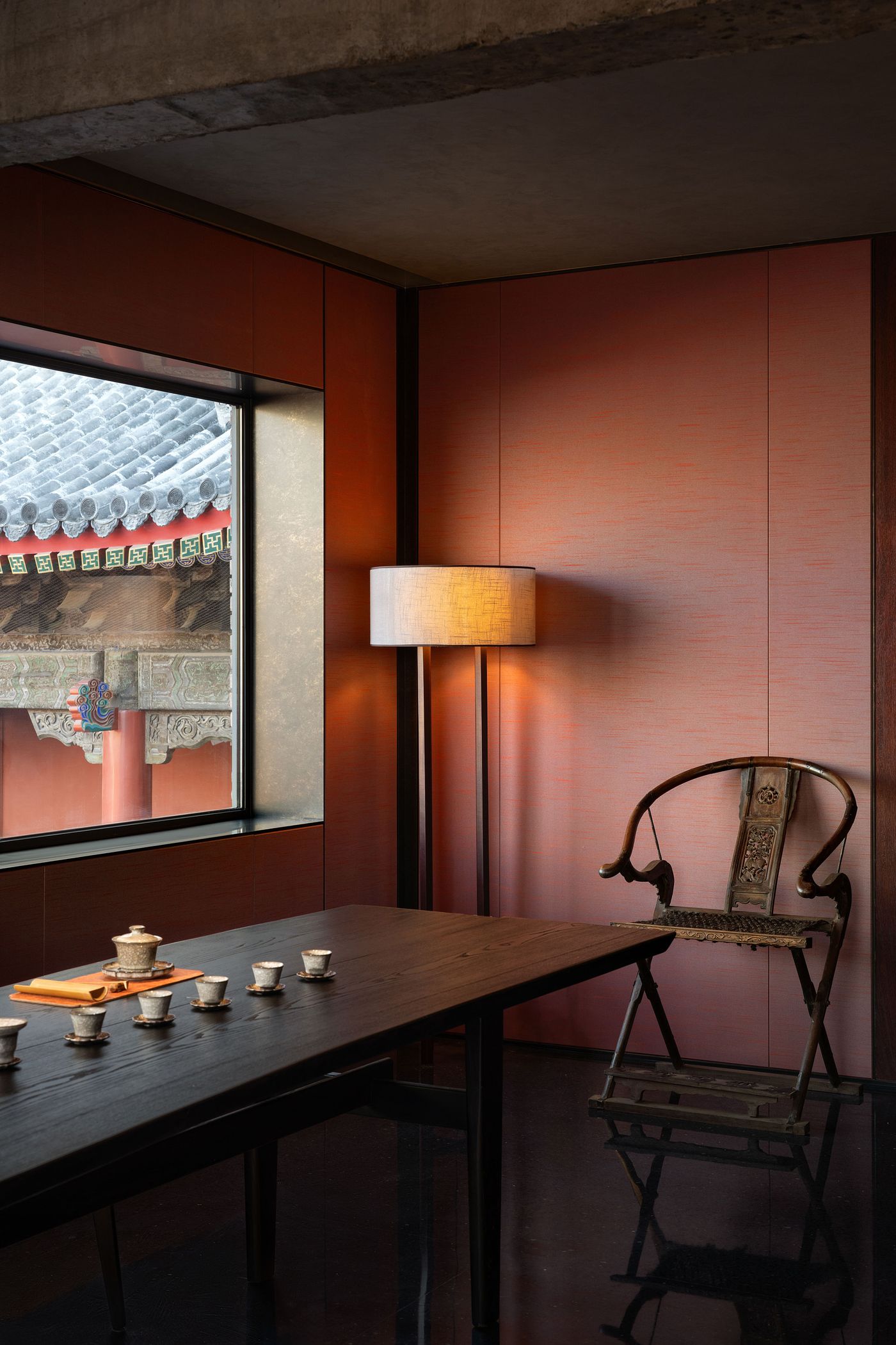 Cozy interior featuring a wooden table with tea sets, a vintage chair, and a soft lamp, with a view of traditional architecture outside. Cozy interior featuring a wooden table with tea sets, a vintage chair, and a soft lamp, with a view of traditional architecture outside.