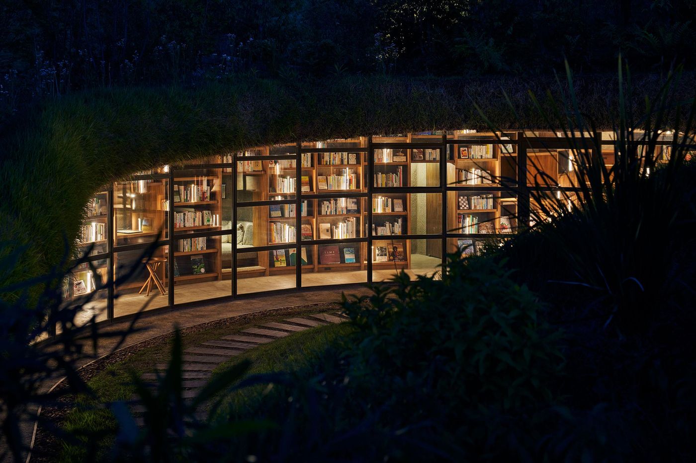 A softly lit modern library nestled in greenery, showcasing shelves filled with books and a cozy reading corner. A softly lit modern library nestled in greenery, showcasing shelves filled with books and a cozy reading corner.