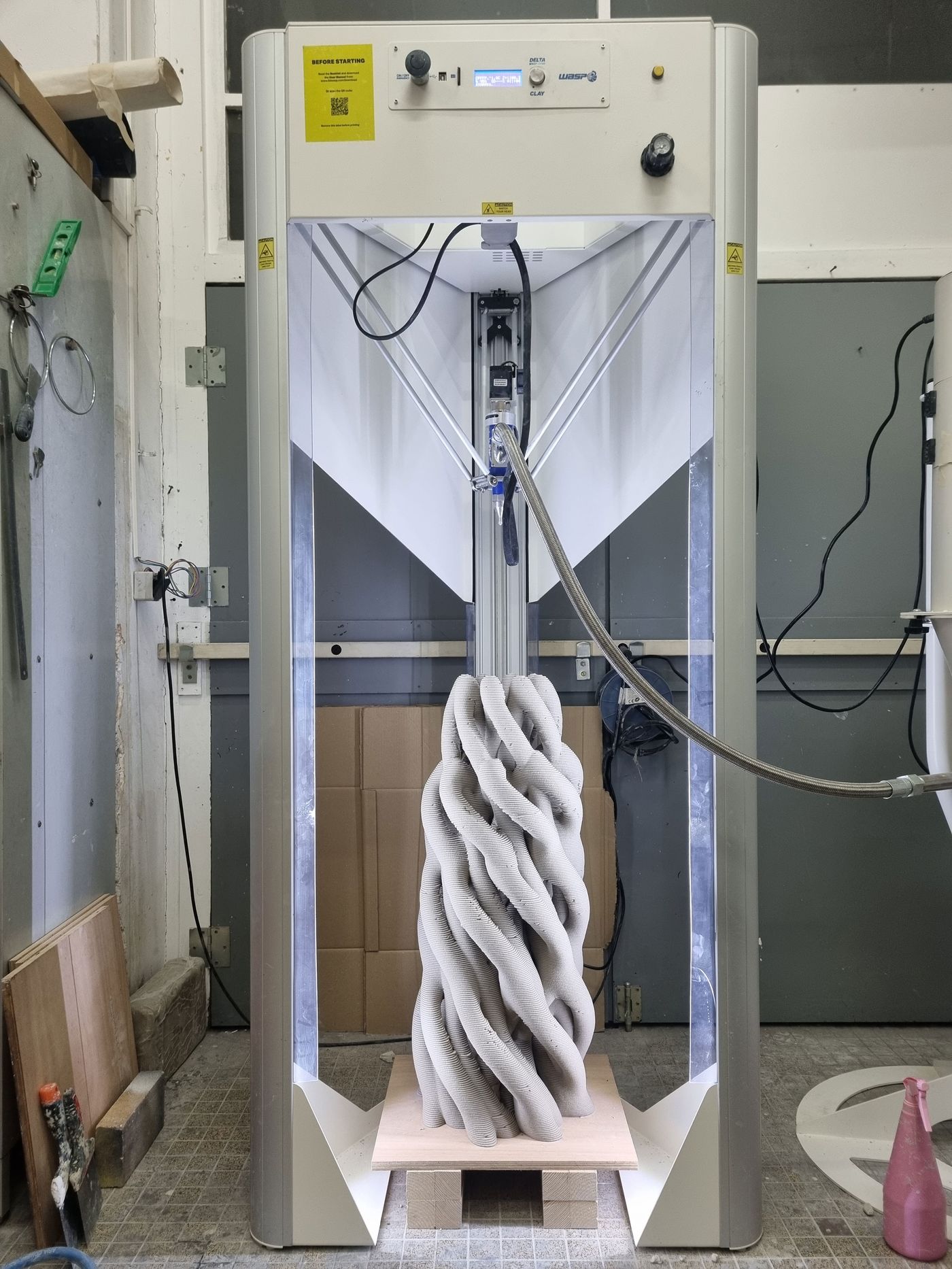 A 3D printer showcasing a textured, twisting sculpture in a workshop setting, with tools and materials nearby.