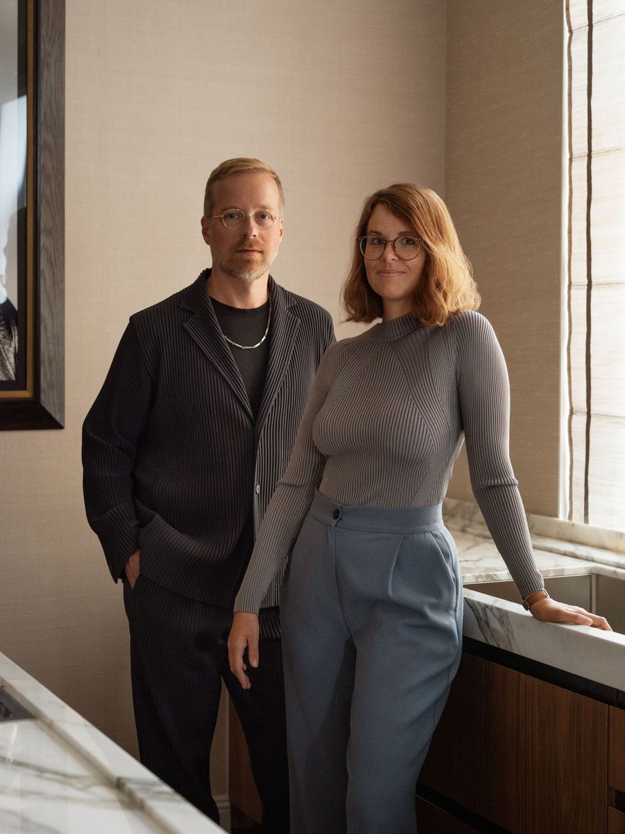 Two people pose in a modern kitchen, showcasing contemporary fashion with textured fabrics and neutral tones. Two people pose in a modern kitchen, showcasing contemporary fashion with textured fabrics and neutral tones.