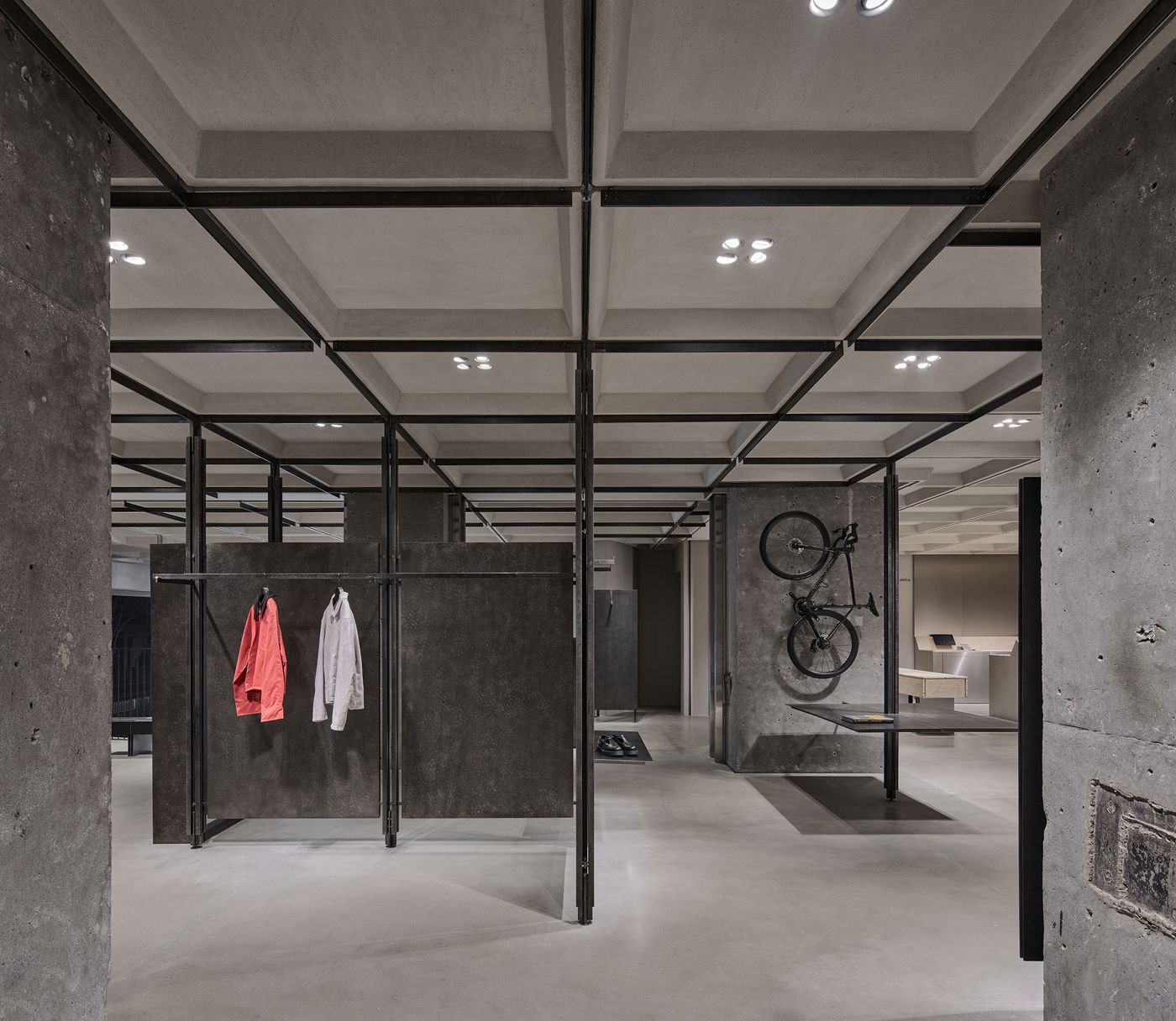 An industrial-style interior with concrete elements, featuring hanging clothing and modern lighting in an open, spacious layout.