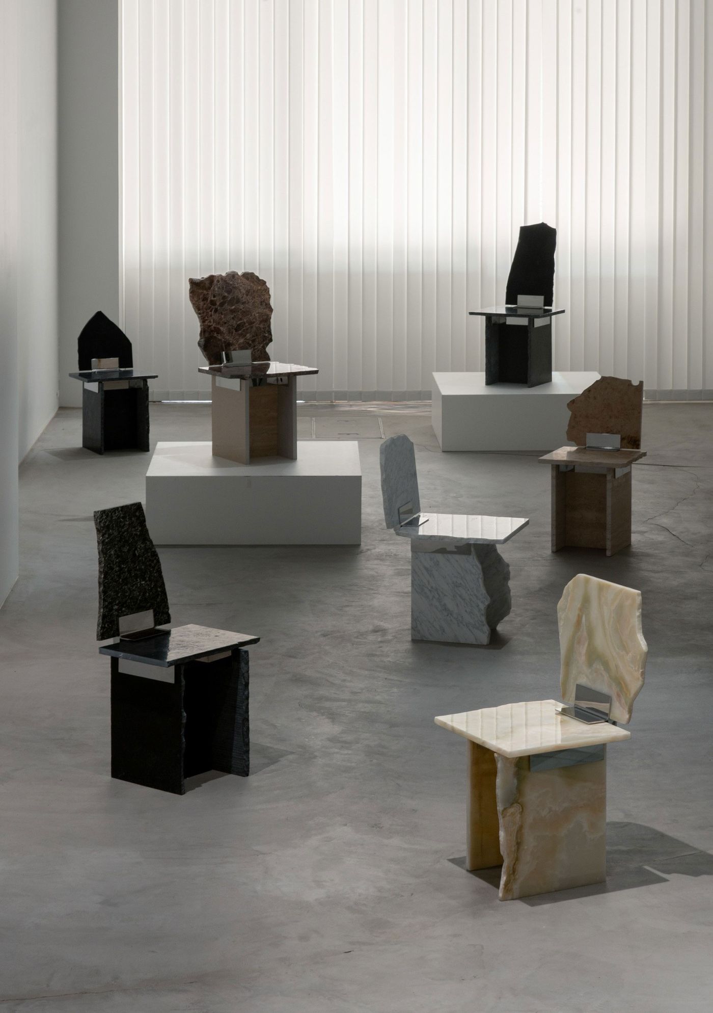 A modern art installation featuring unique sculptural chairs made from various types of stone, displayed in a minimalist gallery. A modern art installation featuring unique sculptural chairs made from various types of stone, displayed in a minimalist gallery.