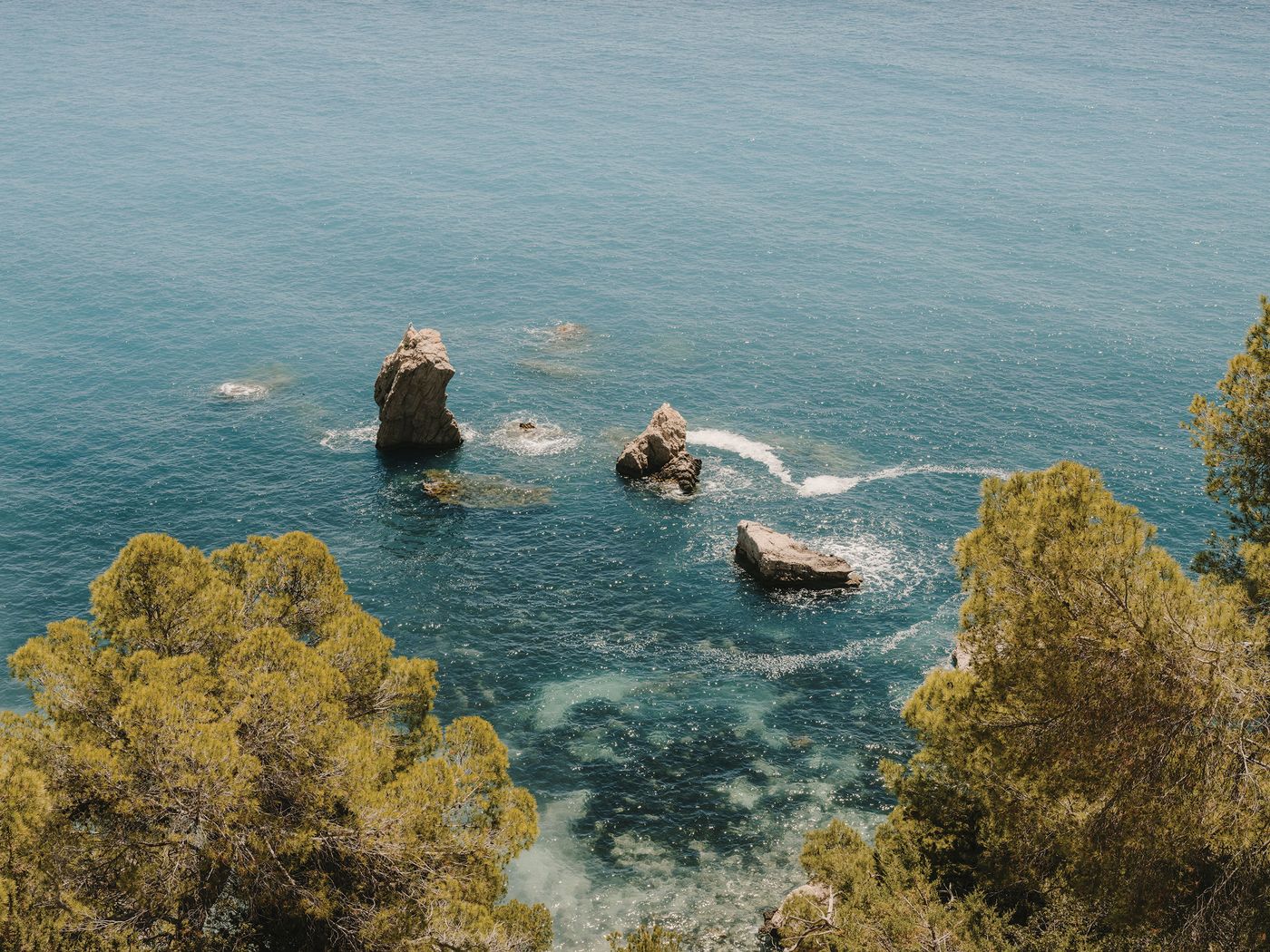 A serene coastal scene featuring three rocky outcrops in turquoise waters, framed by lush green trees along the shoreline. A serene coastal scene featuring three rocky outcrops in turquoise waters, framed by lush green trees along the shoreline.