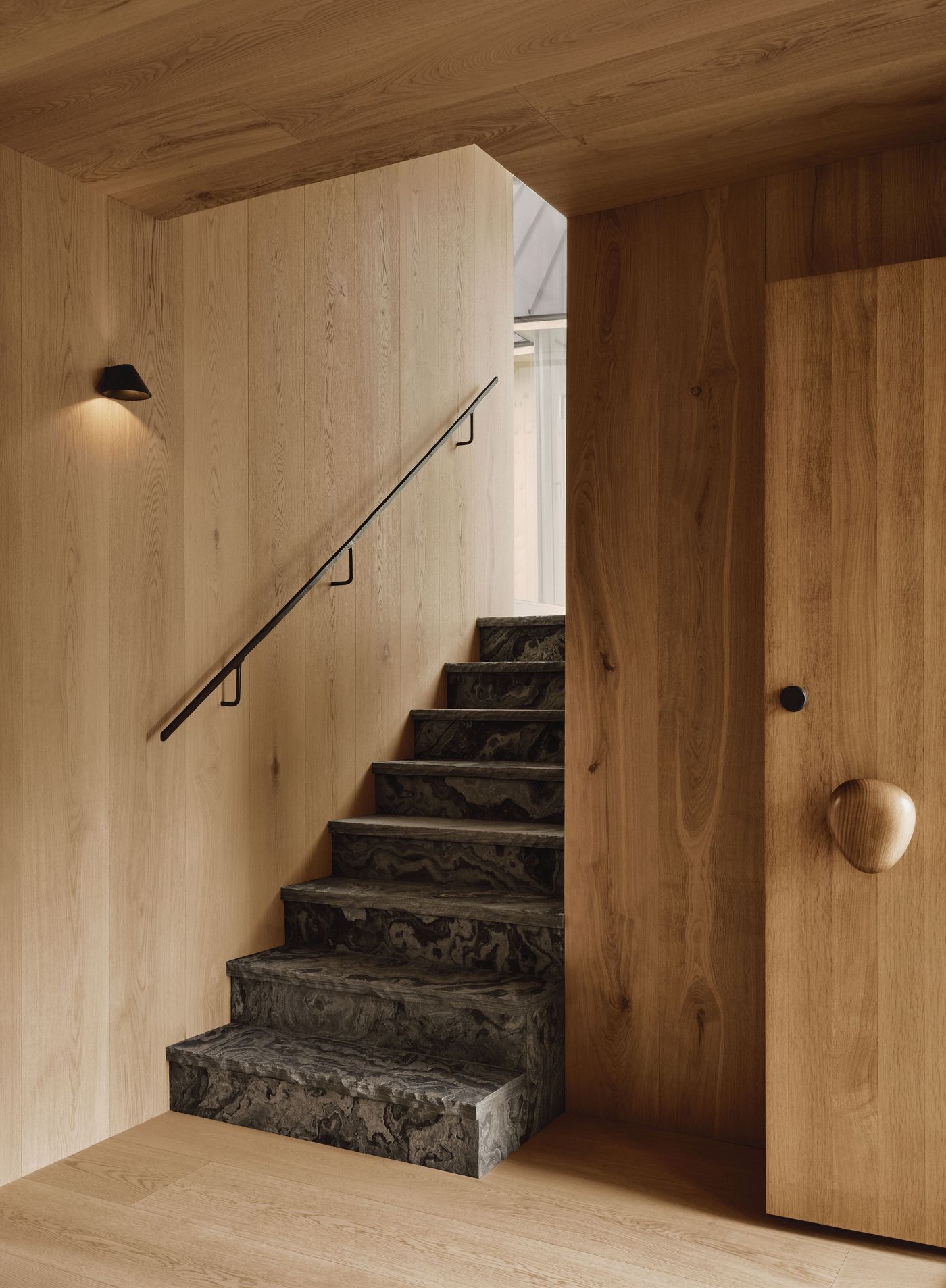 Modern staircase with black textured steps, surrounded by warm wood walls and a stylish wooden door with a unique handle. Modern staircase with black textured steps, surrounded by warm wood walls and a stylish wooden door with a unique handle.
