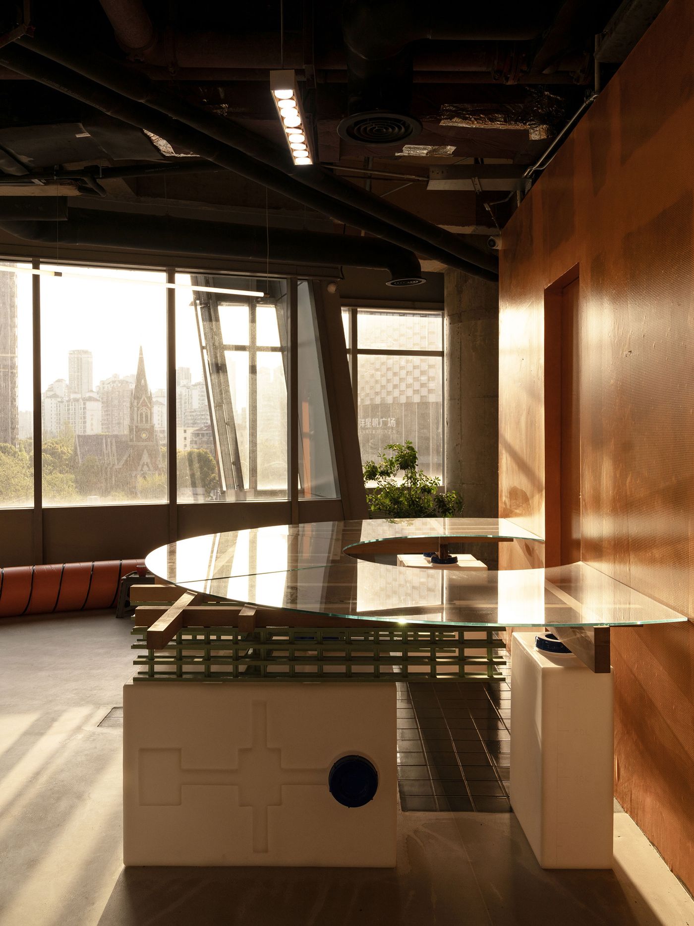 A unique, custom-designed table with a curved glass top and a base featuring a mint green grid and white sculptural elements is showcased in 889 GLO Art Space. The space offers expansive city views through large windows, contrasting the industrial yet refined interior with the urban skyline, embodying a thoughtful blend of brutalist and modern design. A unique, custom-designed table with a curved glass top and a base featuring a mint green grid and white sculptural elements is showcased in 889 GLO Art Space. The space offers expansive city views through large windows, contrasting the industrial yet refined interior with the urban skyline, embodying a thoughtful blend of brutalist and modern design.