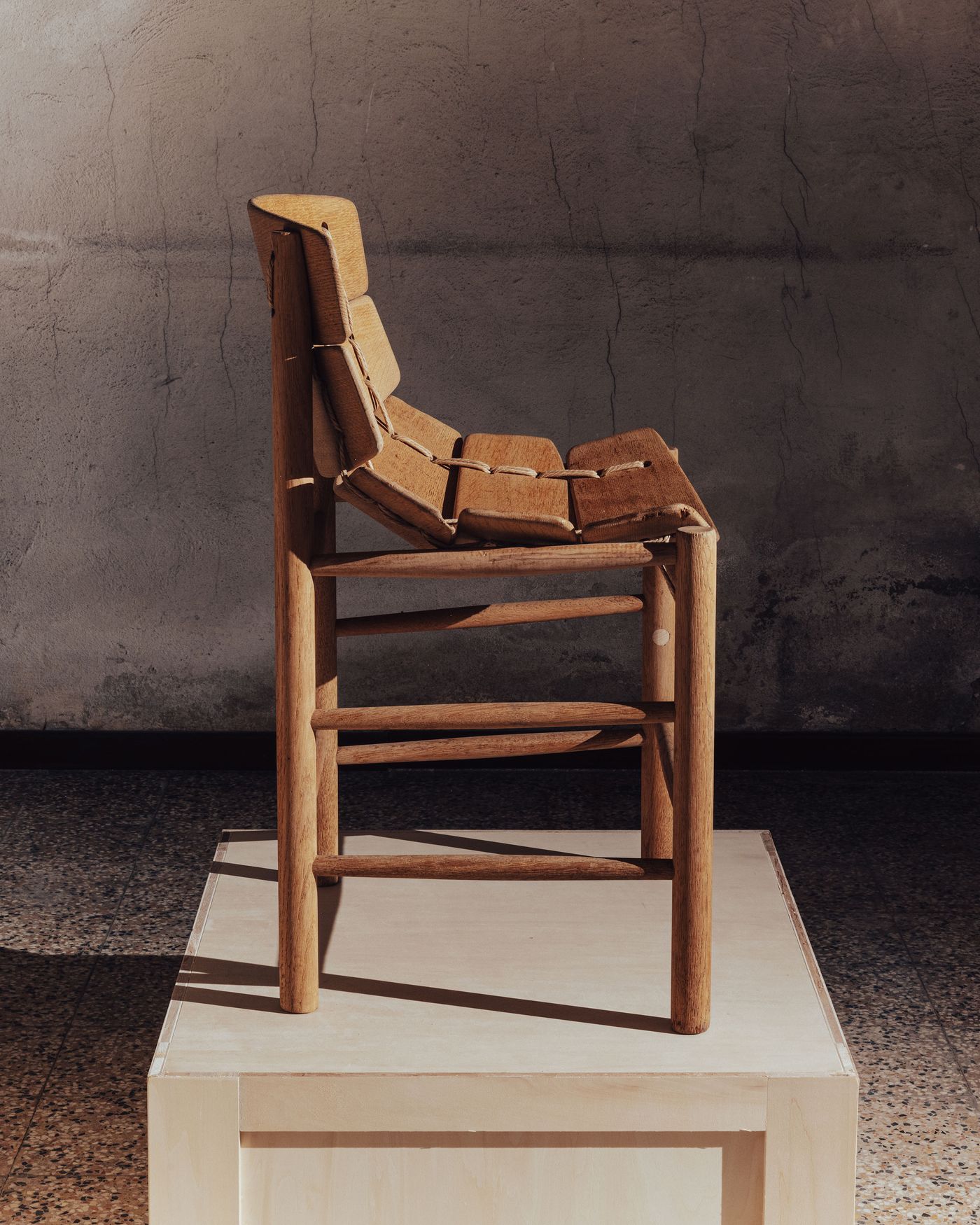 A wooden chair with a minimalist design, showcasing a structured seat and backrest, displayed on a light pedestal. A wooden chair with a minimalist design, showcasing a structured seat and backrest, displayed on a light pedestal.