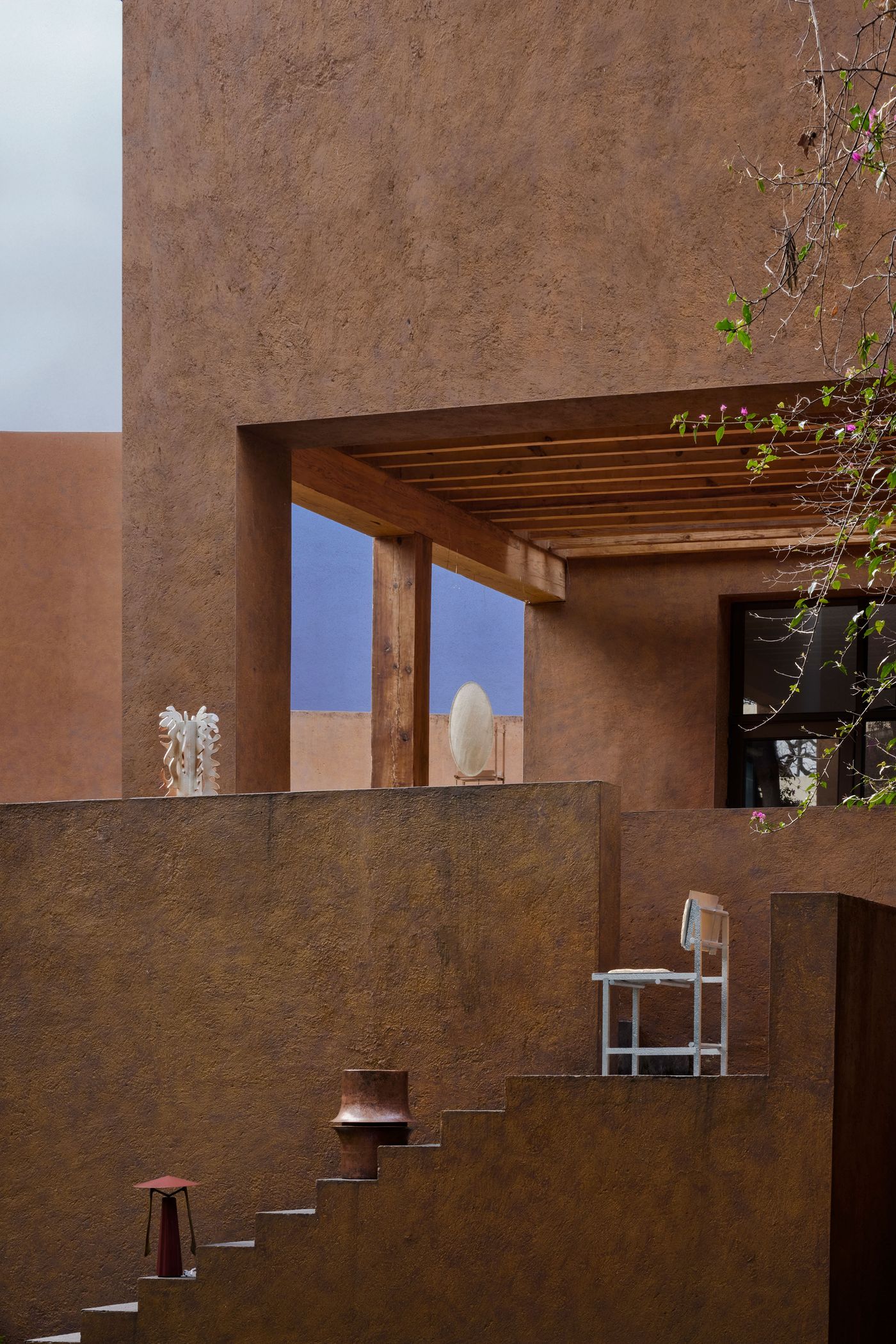 A modern architectural design featuring textured brown walls, wooden beams, a white chair, and decorative elements in a serene outdoor space.