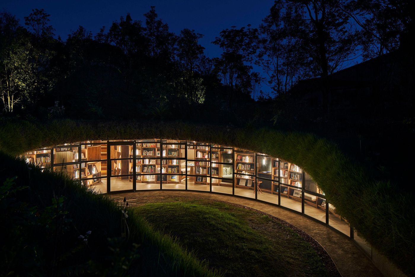 A cozy, curved library nestled in green hills, illuminated at night, surrounded by trees and softly glowing bookshelves. A cozy, curved library nestled in green hills, illuminated at night, surrounded by trees and softly glowing bookshelves.
