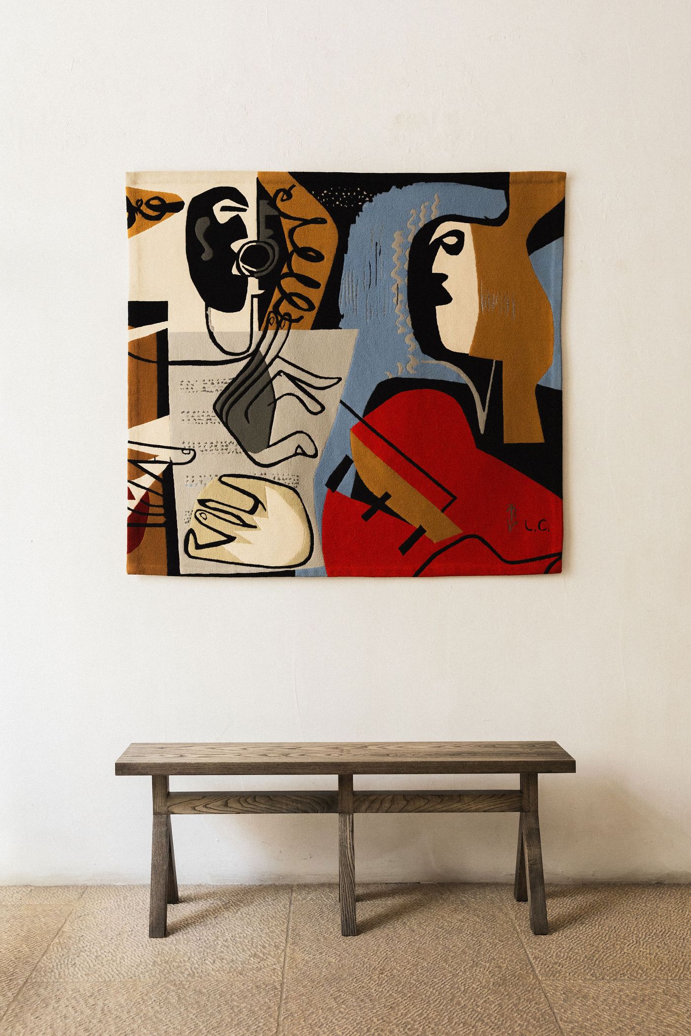 A vibrant abstract tapestry, on view at Galeria Tapeçarias de Portalegre, dominates a plain white wall above a rustic wooden bench. The artwork features bold, cubist-inspired forms in black, white, brown, and a striking red, depicting musical elements and abstract figures. The composition's clean lines and minimalist pairing allow the intricate textile to be the focal point. A vibrant abstract tapestry, on view at Galeria Tapeçarias de Portalegre, dominates a plain white wall above a rustic wooden bench. The artwork features bold, cubist-inspired forms in black, white, brown, and a striking red, depicting musical elements and abstract figures. The composition's clean lines and minimalist pairing allow the intricate textile to be the focal point.