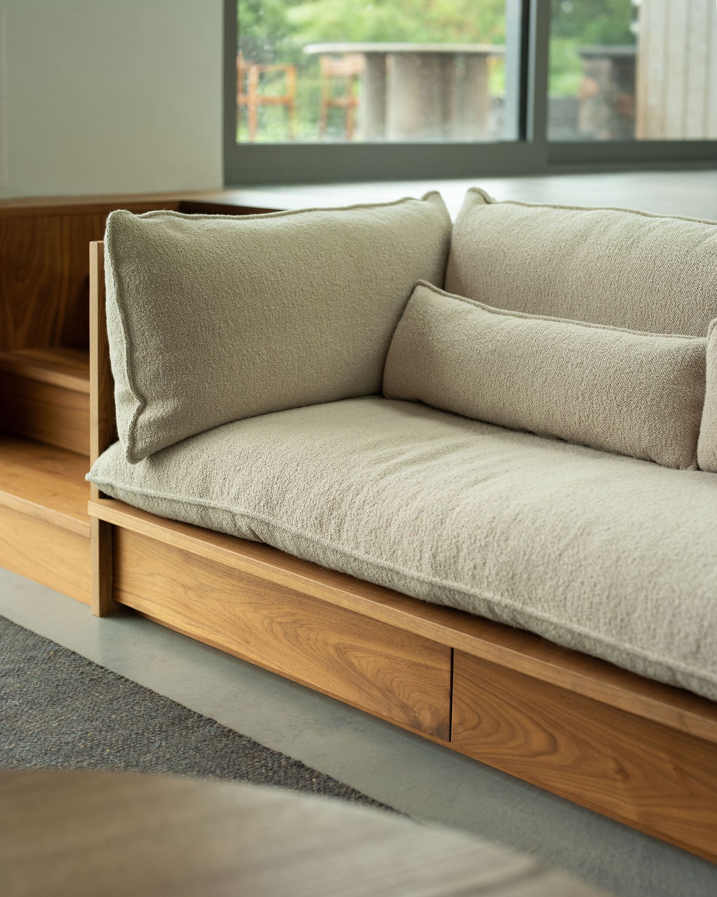 A cozy beige sofa with textured cushions rests against a large window, showcasing a serene outdoor view.