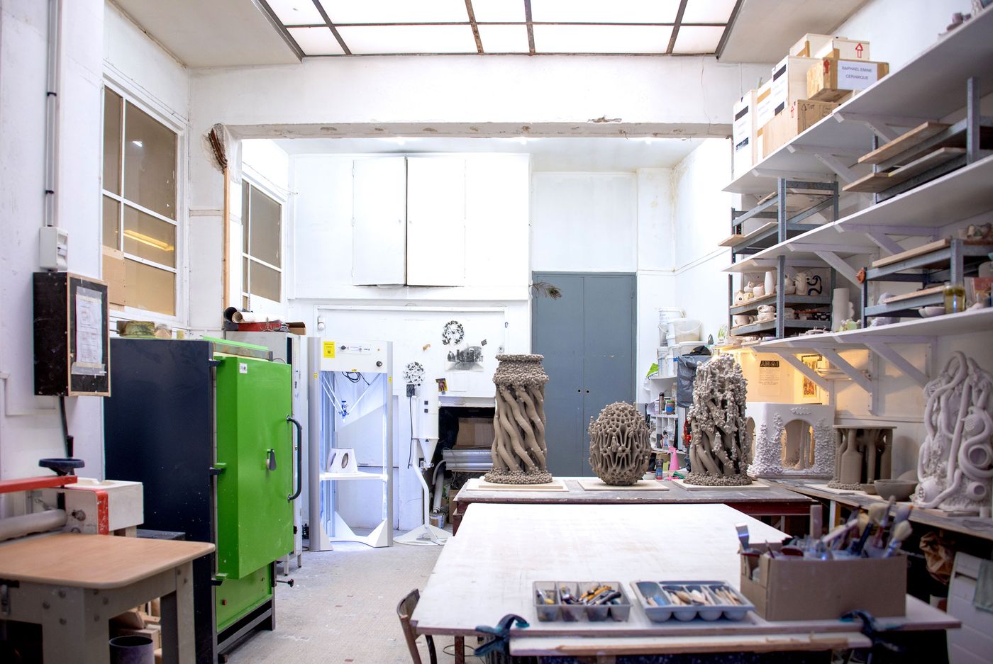 A bright artist's studio featuring sculpting tools, storage shelves, and unique clay sculptures displayed on a large table. A bright artist's studio featuring sculpting tools, storage shelves, and unique clay sculptures displayed on a large table.