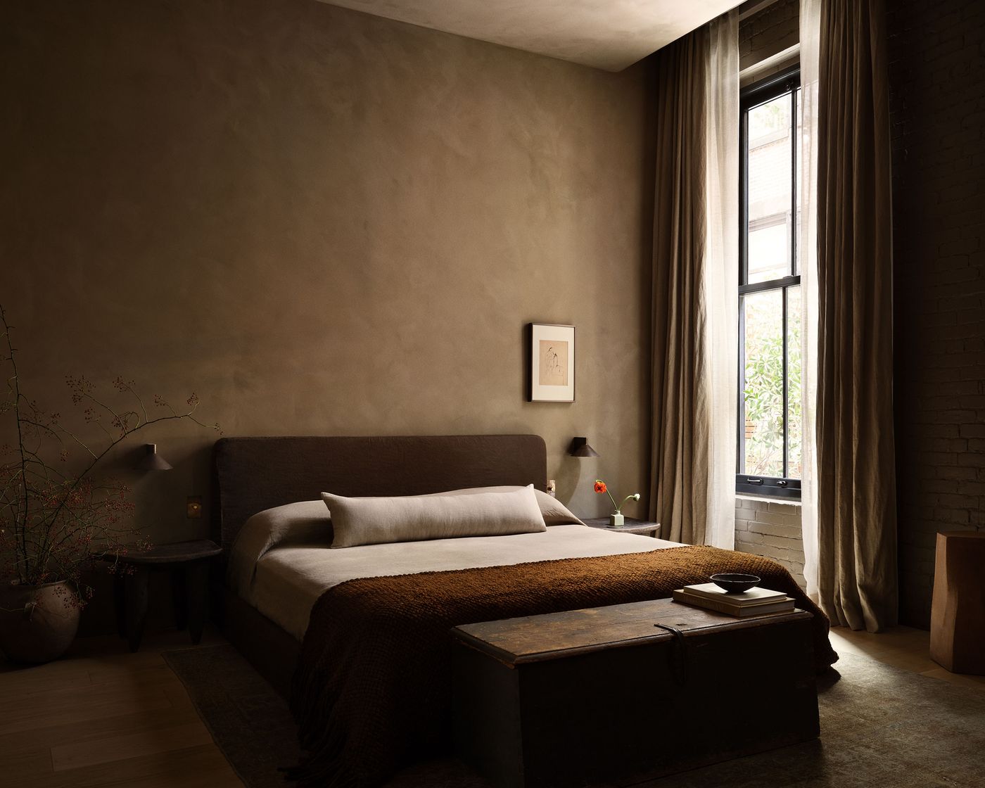 A serene bedroom featuring a minimalist wooden bed with a brown throw, soft lighting, and a window with flowing curtains. A serene bedroom featuring a minimalist wooden bed with a brown throw, soft lighting, and a window with flowing curtains.