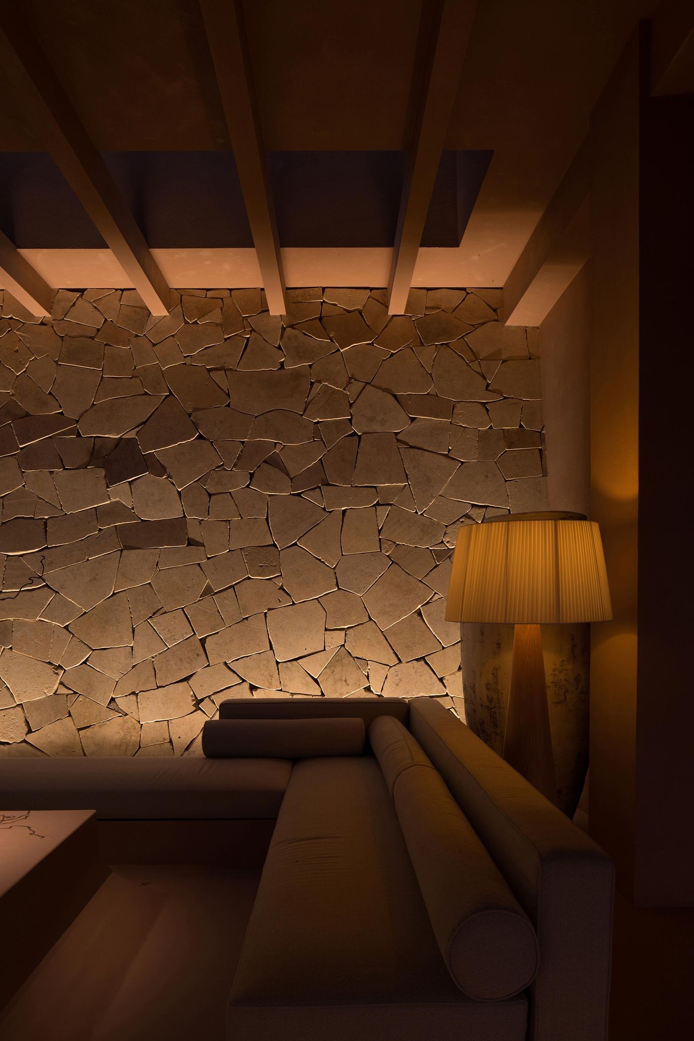 A cozy, dimly lit living space featuring a modern sofa, a textured stone wall, and a stylish lamp, creating a warm atmosphere. A cozy, dimly lit living space featuring a modern sofa, a textured stone wall, and a stylish lamp, creating a warm atmosphere.