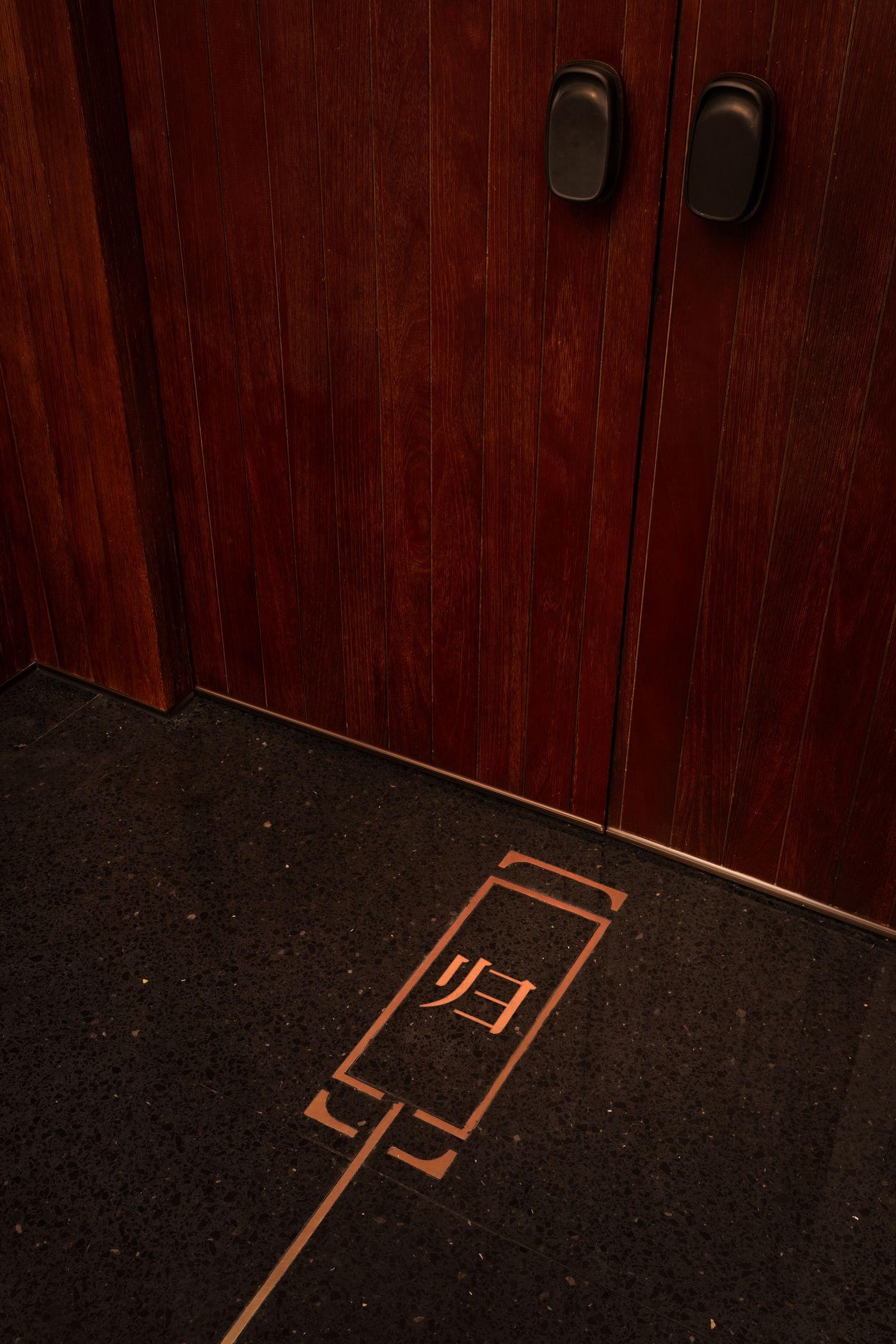 Close-up of an elevator door with wooden panels and a floor marker indicating the elevator location, featuring a simple icon and Chinese characters. Close-up of an elevator door with wooden panels and a floor marker indicating the elevator location, featuring a simple icon and Chinese characters.