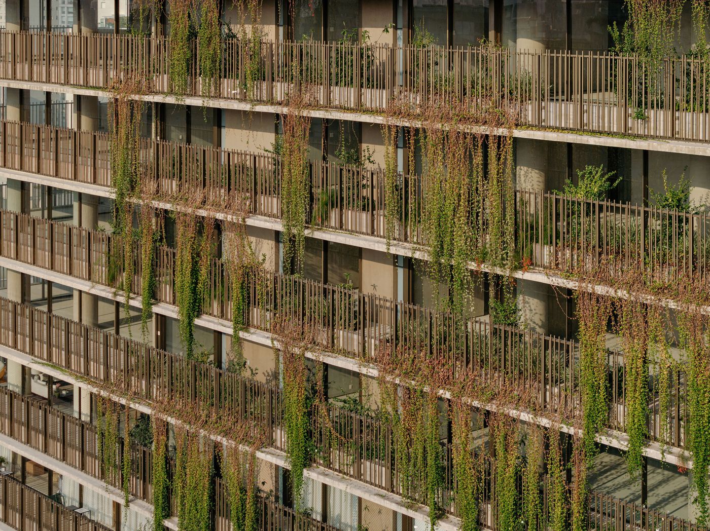A close-up of this project's facade reveals a textured tapestry of vertical metal balustrades and cascading green vines that soften the concrete balconies. This intricate biophilic layering showcases the building's living skin, blurring the line between architecture and nature in a vibrant display. A close-up of this project's facade reveals a textured tapestry of vertical metal balustrades and cascading green vines that soften the concrete balconies. This intricate biophilic layering showcases the building's living skin, blurring the line between architecture and nature in a vibrant display.