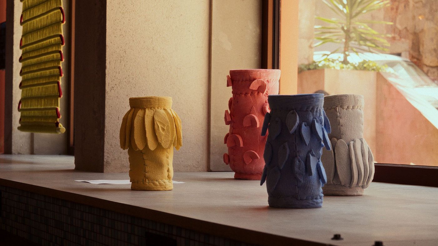 A close-up of decorative, tactile ceramic vases displayed on a window ledge, likely from the JAM Hotel during Lisbon Design Week. Three sculptural vessels in vibrant yellow, coral, and blue feature repetitive, organic textures and attached relief elements, highlighting a handcrafted, modern aesthetic. Natural light from a large window illuminates their rich, matte surfaces A close-up of decorative, tactile ceramic vases displayed on a window ledge, likely from the JAM Hotel during Lisbon Design Week. Three sculptural vessels in vibrant yellow, coral, and blue feature repetitive, organic textures and attached relief elements, highlighting a handcrafted, modern aesthetic. Natural light from a large window illuminates their rich, matte surfaces