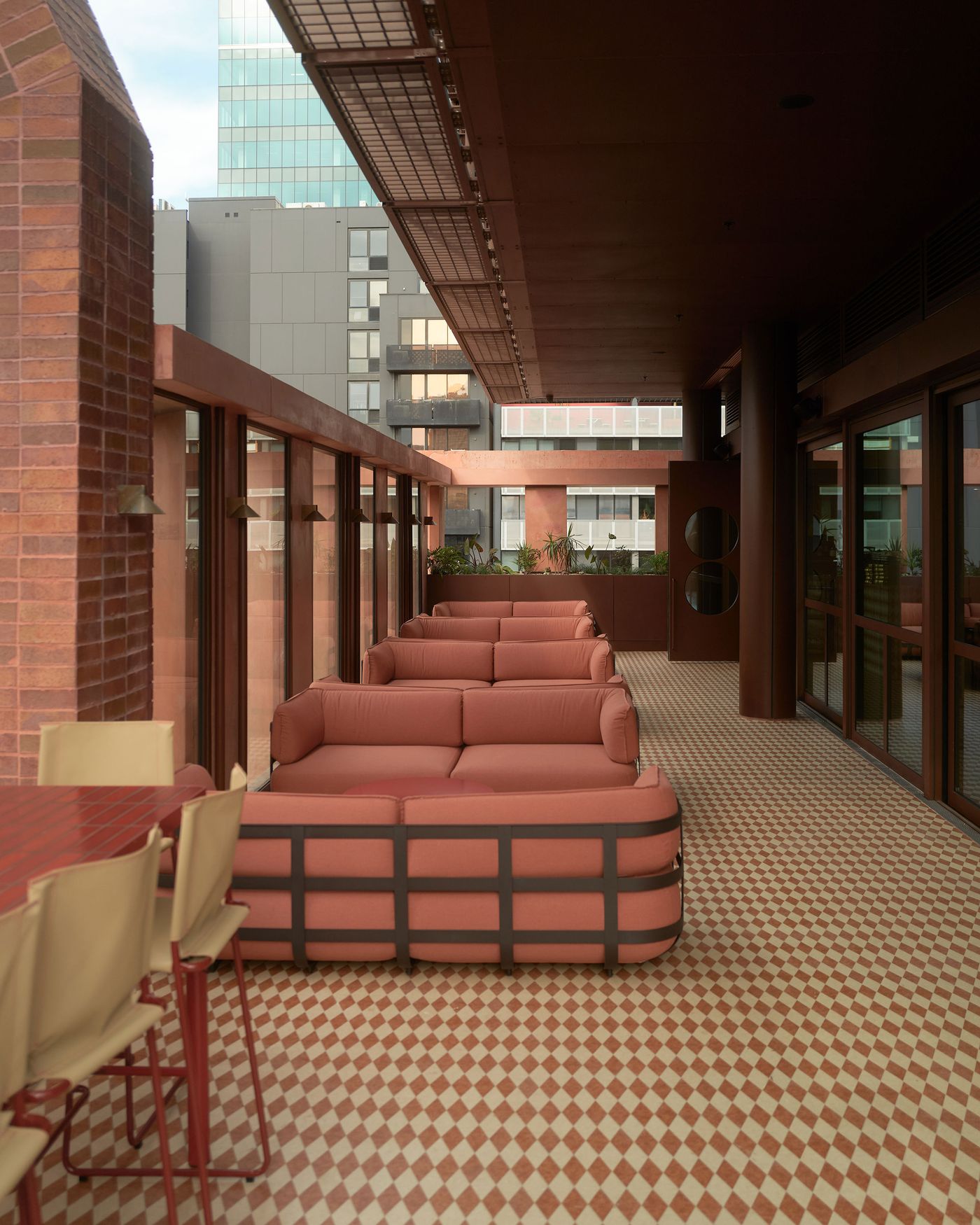 A stylish rooftop lounge featuring pink sofas, a patterned floor, and panoramic windows with views of modern city buildings. A stylish rooftop lounge featuring pink sofas, a patterned floor, and panoramic windows with views of modern city buildings.