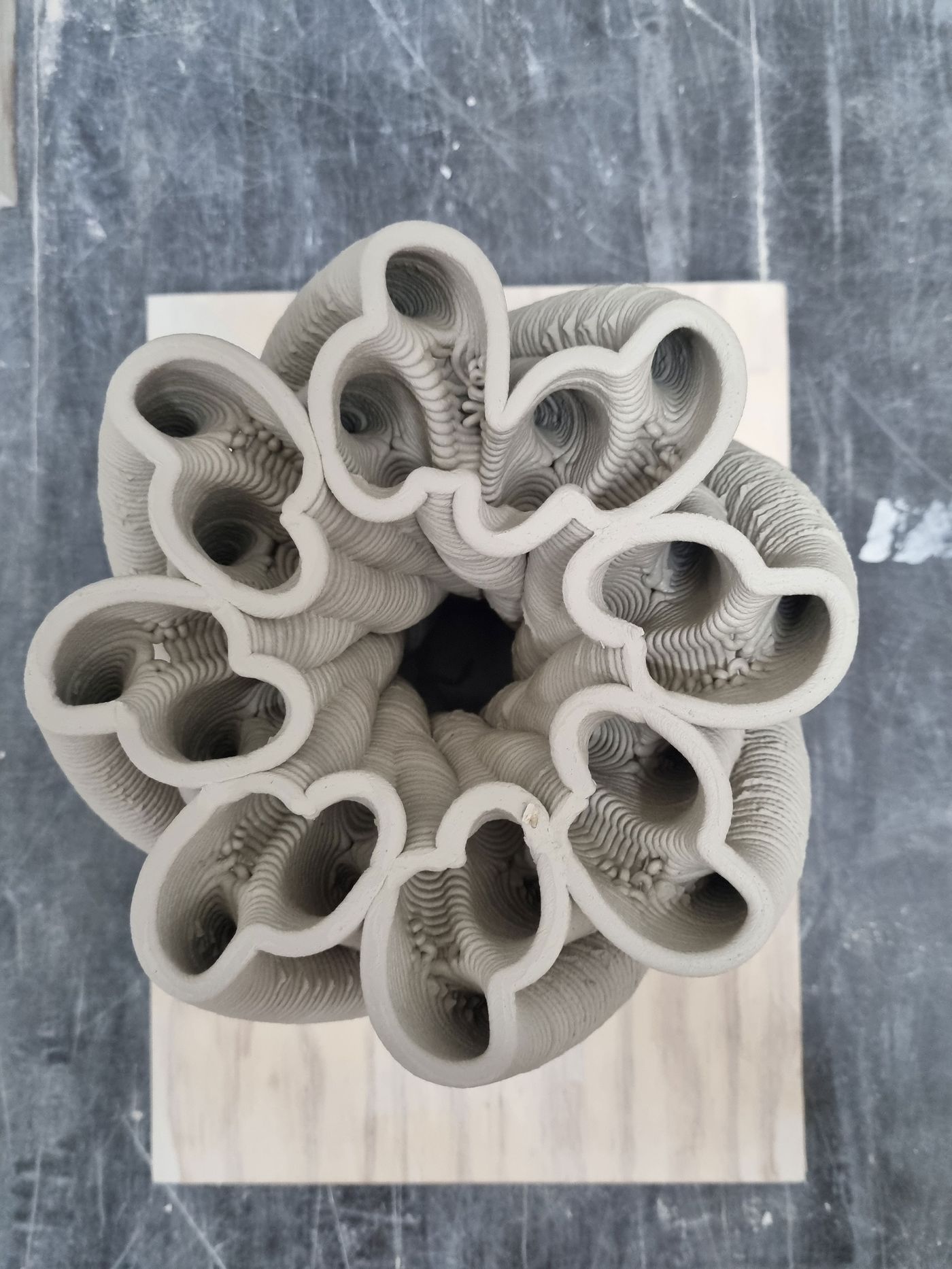 Top view of a textured, sculptural ceramic piece with wavy, intertwined shapes in light gray, resting on a wooden base.