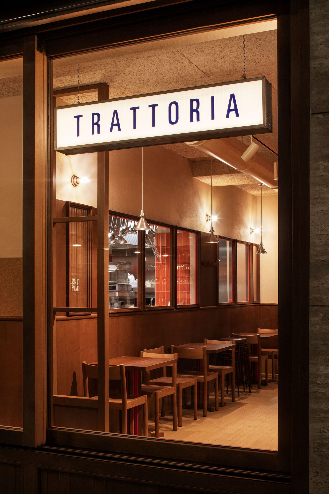 A warm evening view into Santo Palato by Naessi Studio, highlighted by the glowing "TRATTORIA" sign. The restaurant's interior is visible through large windows, showcasing cozy wooden tables, banquette seating, and industrial pendant lights. The warm lighting and inviting decor project an authentic and modern Roman trattoria ambiance. A warm evening view into Santo Palato by Naessi Studio, highlighted by the glowing "TRATTORIA" sign. The restaurant's interior is visible through large windows, showcasing cozy wooden tables, banquette seating, and industrial pendant lights. The warm lighting and inviting decor project an authentic and modern Roman trattoria ambiance.