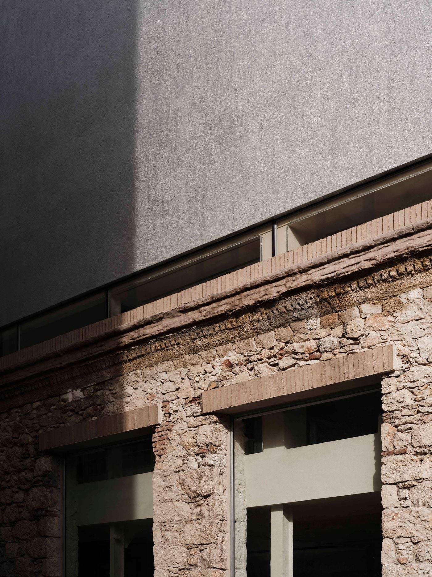 Strong sunlight accentuates the meeting of old and new on Castor Place’s exterior: rough stonework and brick detailing below, a textured pale volume above, and a narrow band of glazing between them. Deep shadows sharpen the façade’s layered construction and contrasting surface treatments. Strong sunlight accentuates the meeting of old and new on Castor Place’s exterior: rough stonework and brick detailing below, a textured pale volume above, and a narrow band of glazing between them. Deep shadows sharpen the façade’s layered construction and contrasting surface treatments.