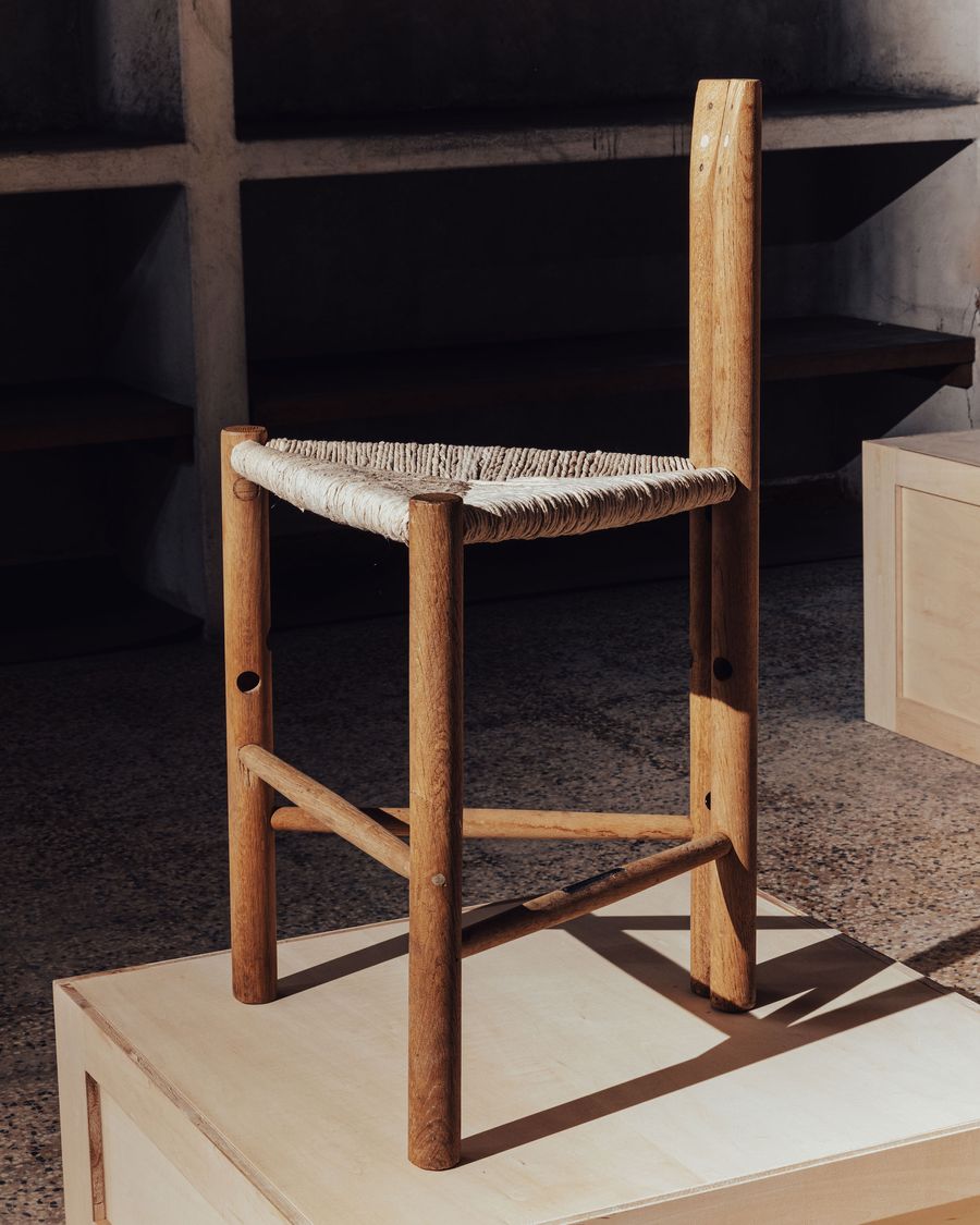 A minimalist wooden chair with a woven seat, displayed on a light wooden pedestal in a stylish, modern setting. A minimalist wooden chair with a woven seat, displayed on a light wooden pedestal in a stylish, modern setting.