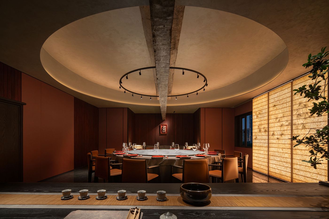 Modern dining room with a circular table, elegant decor, warm lighting, and a serene ambiance created by textured walls and natural elements. Modern dining room with a circular table, elegant decor, warm lighting, and a serene ambiance created by textured walls and natural elements.