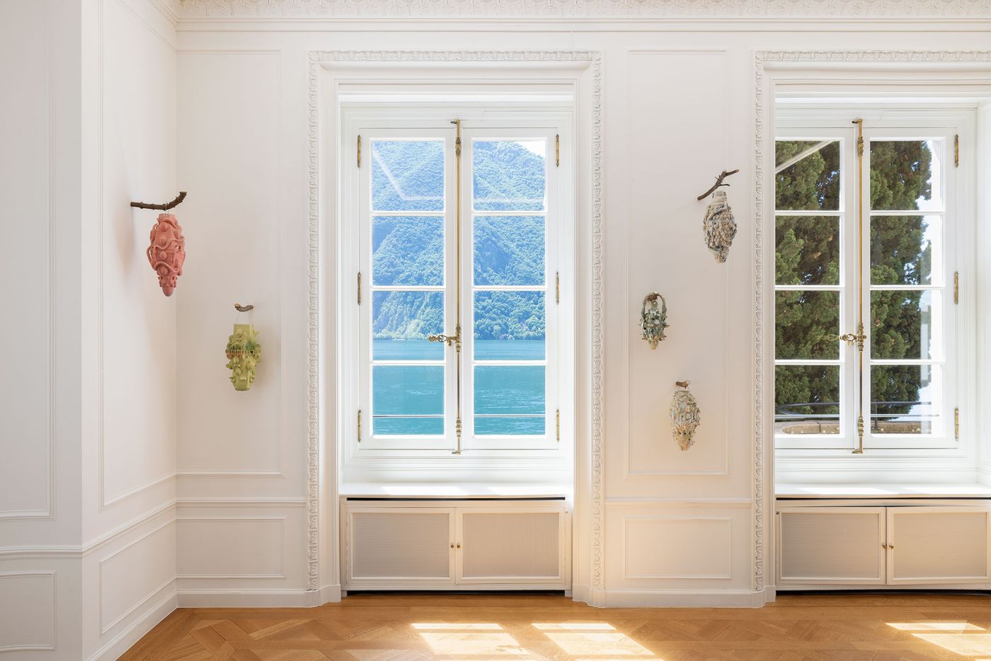 Two windows reveal a scenic view of mountains and water, adorned with colorful art pieces on white walls, showcasing modern design. Two windows reveal a scenic view of mountains and water, adorned with colorful art pieces on white walls, showcasing modern design.
