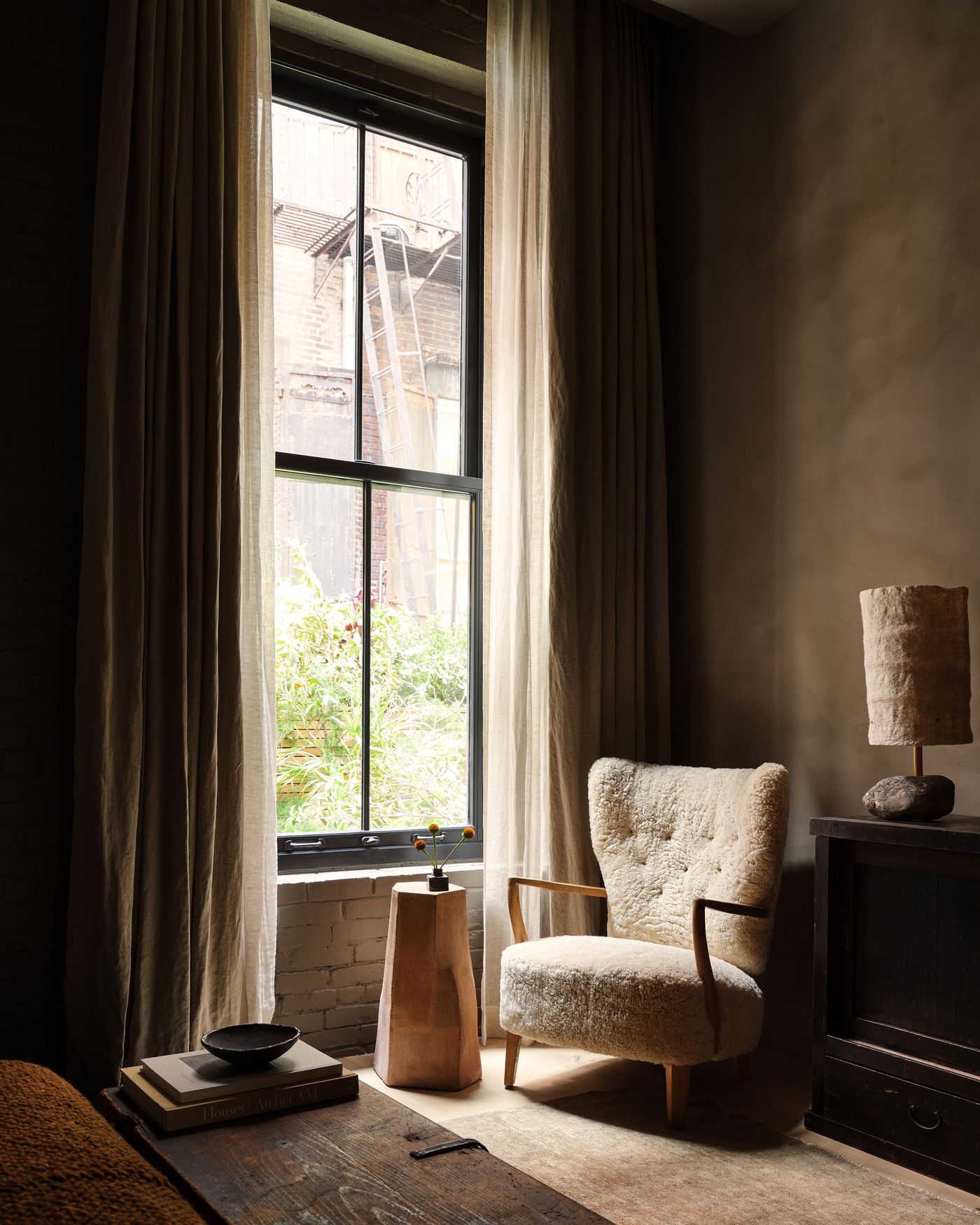 Cozy interior featuring a fluffy armchair by a large window adorned with light curtains, a wooden side table, and decorative accents. Cozy interior featuring a fluffy armchair by a large window adorned with light curtains, a wooden side table, and decorative accents.
